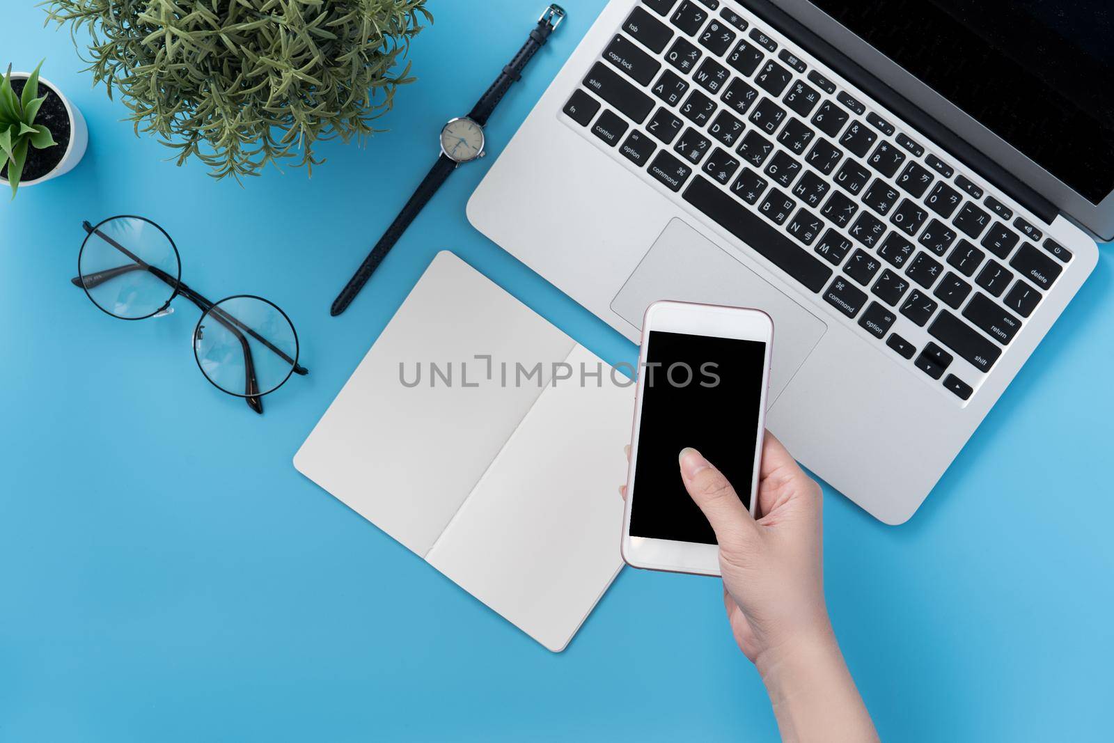 Concept of home office table with fashion accessories, minimal interior with a woman holding smartphone, flat lay, copy space, top view, mockup