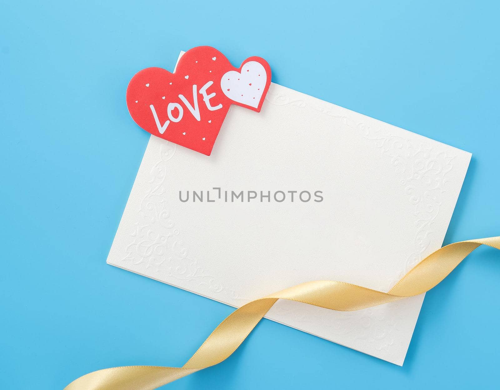 Beautiful greeting card with golden ribbon for Valentine's day, anniversary, mother's day and birthday on blue background, copyspace, topview, mockup, flatlay