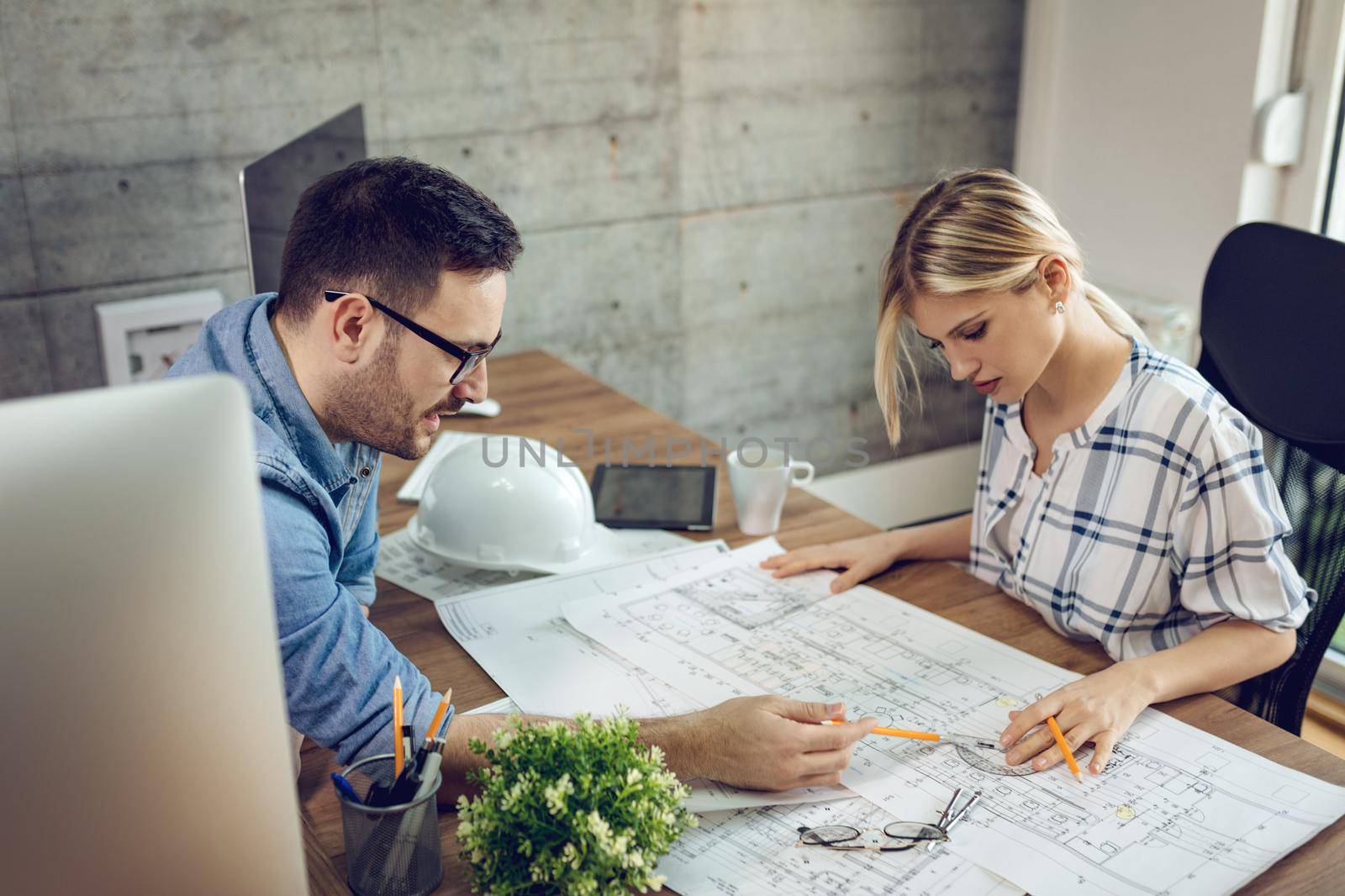 Young pensive architect colleagues analyzing blueprints and talking about him at the office.