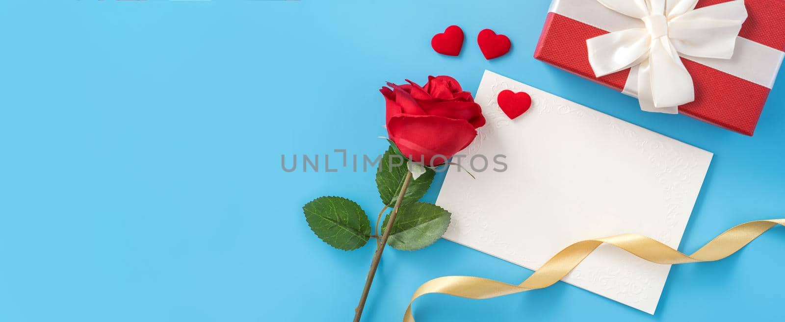 Beautiful greeting card with golden ribbon for Valentine's day, anniversary, mother's day and birthday on blue background, copyspace, topview, mockup, flatlay by ROMIXIMAGE