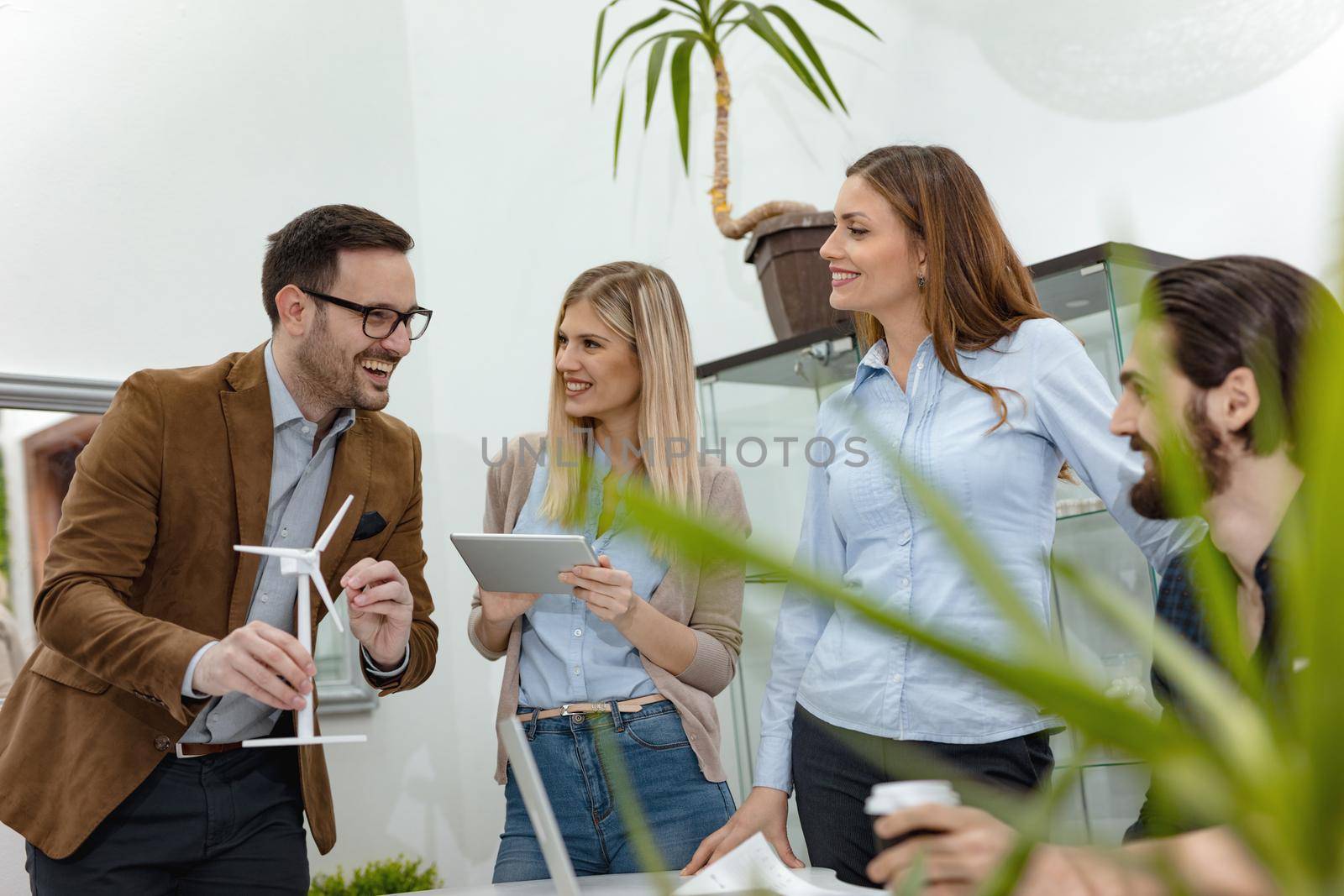 A team of smart qualified skilled young engineers discussing about the project of alternative energy and one of them holding the tiny model of windmill turbine, and explaining how it working. 