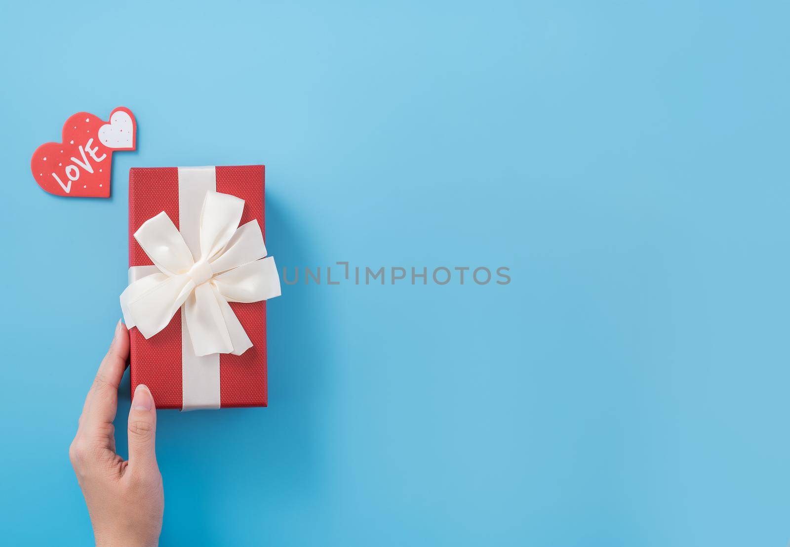A young woman is giving a gift with greeting on blue background, concept of holiday and celebrate for festival surprising, copyspace, topview