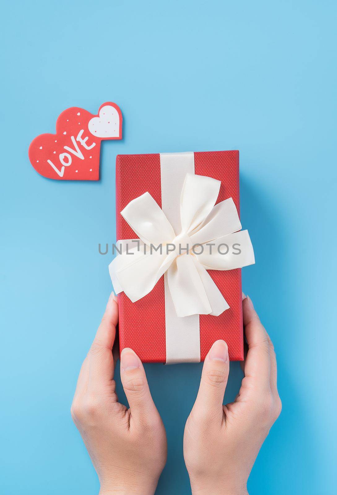 A young woman is giving a gift with greeting on blue background, concept of holiday and celebrate for festival surprising, copyspace, topview