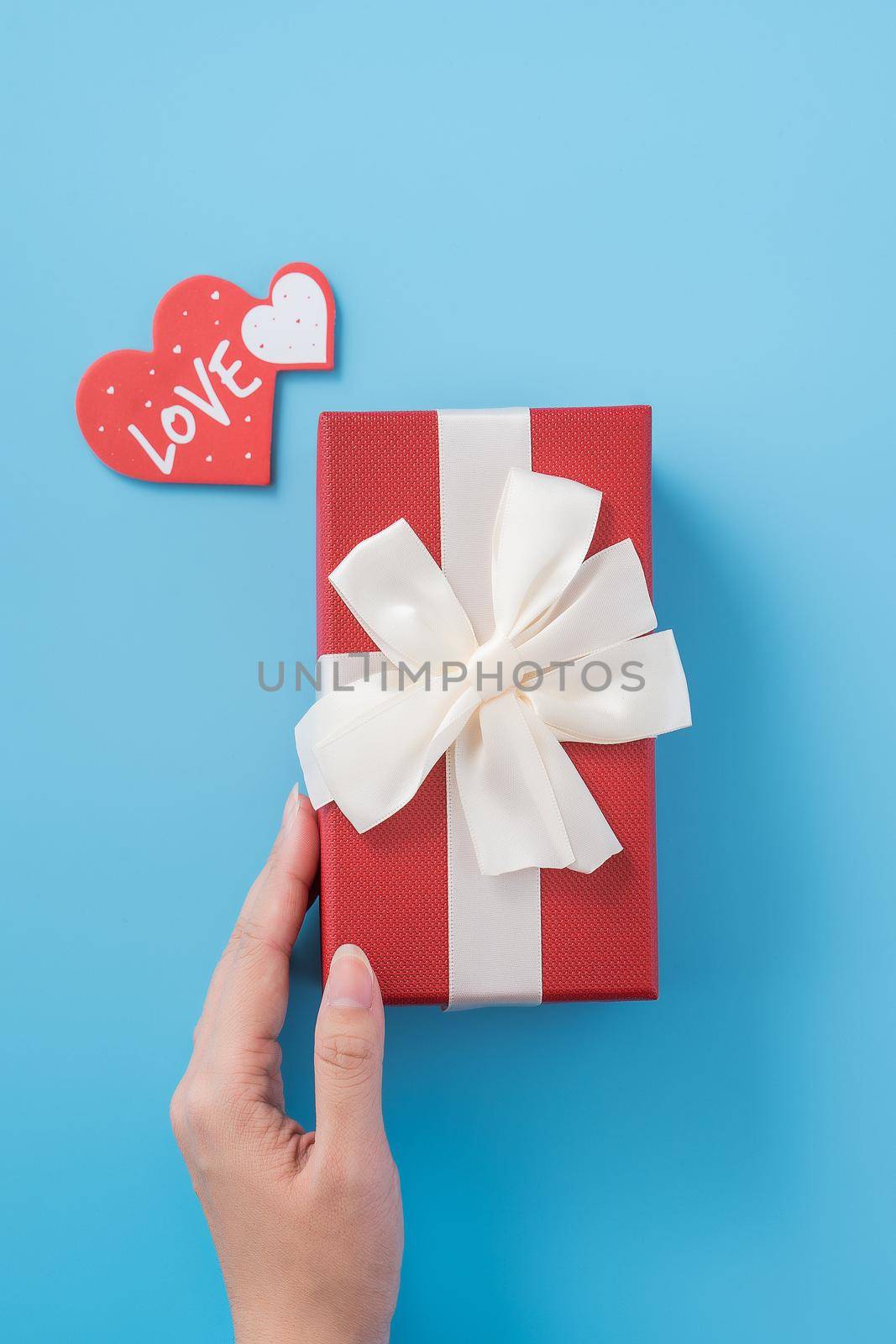 A young woman is giving a gift with greeting on blue background, concept of holiday and celebrate for festival surprising, copyspace, topview