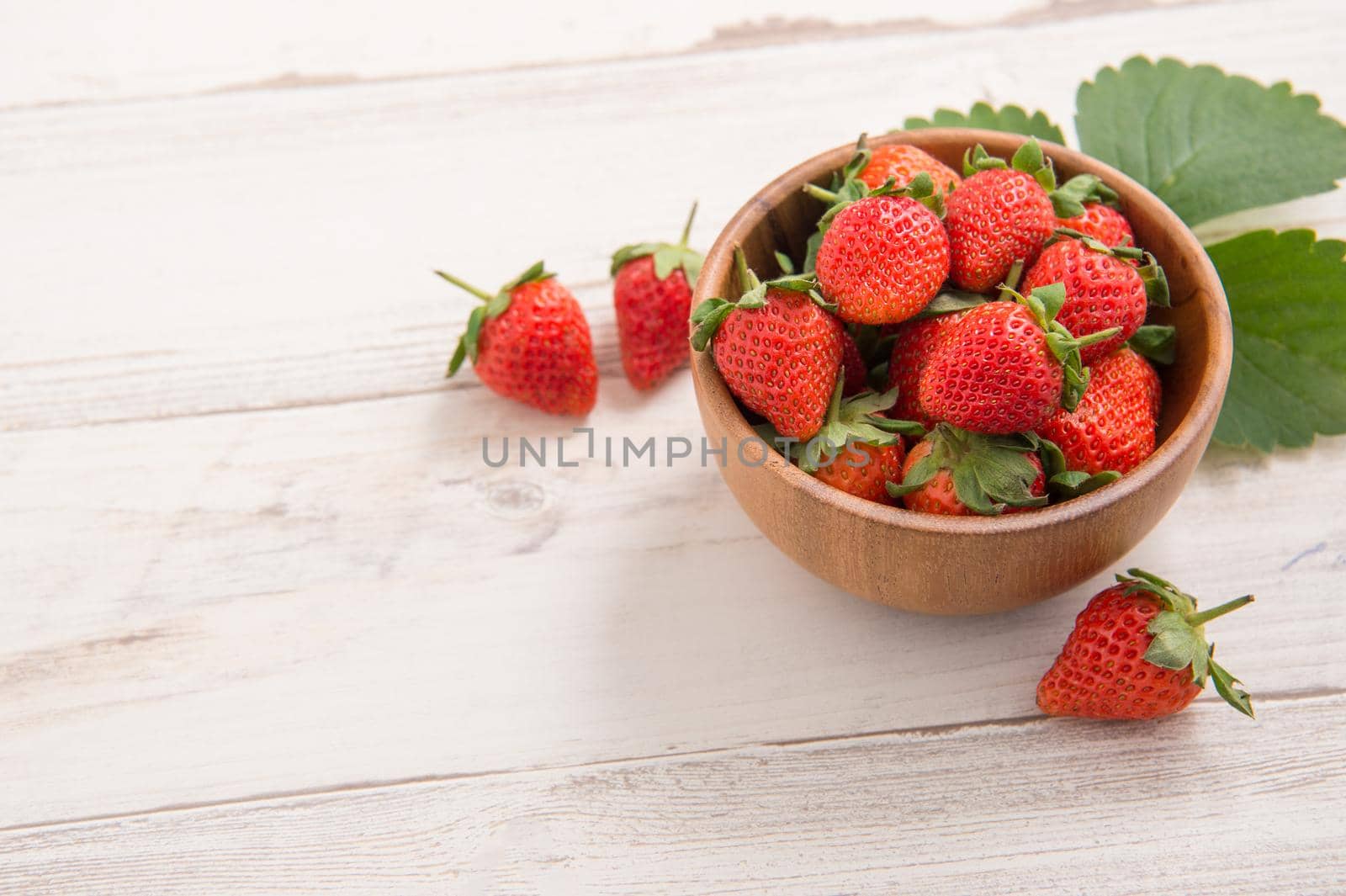 A bowl of beautiful and delicious strawberries isolated on a light wooden background, closeup, topview, copyspace.