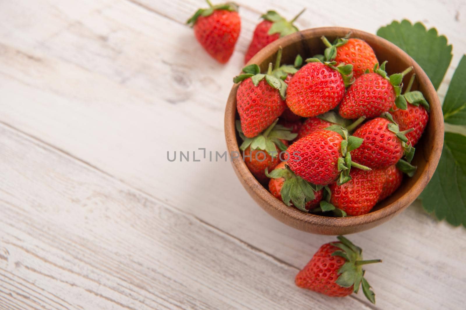 A bowl of beautiful and delicious strawberries isolated on a light wooden background, closeup, topview, copyspace.