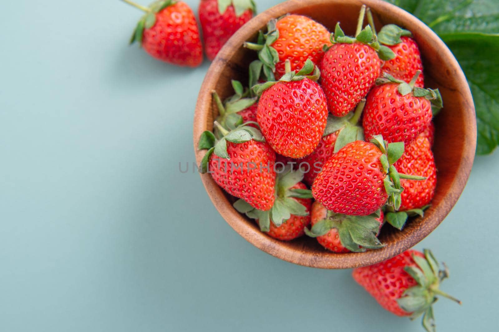 A bowl of beautiful and delicious strawberries isolated on a blue-green background, closeup, topview, copyspace.
