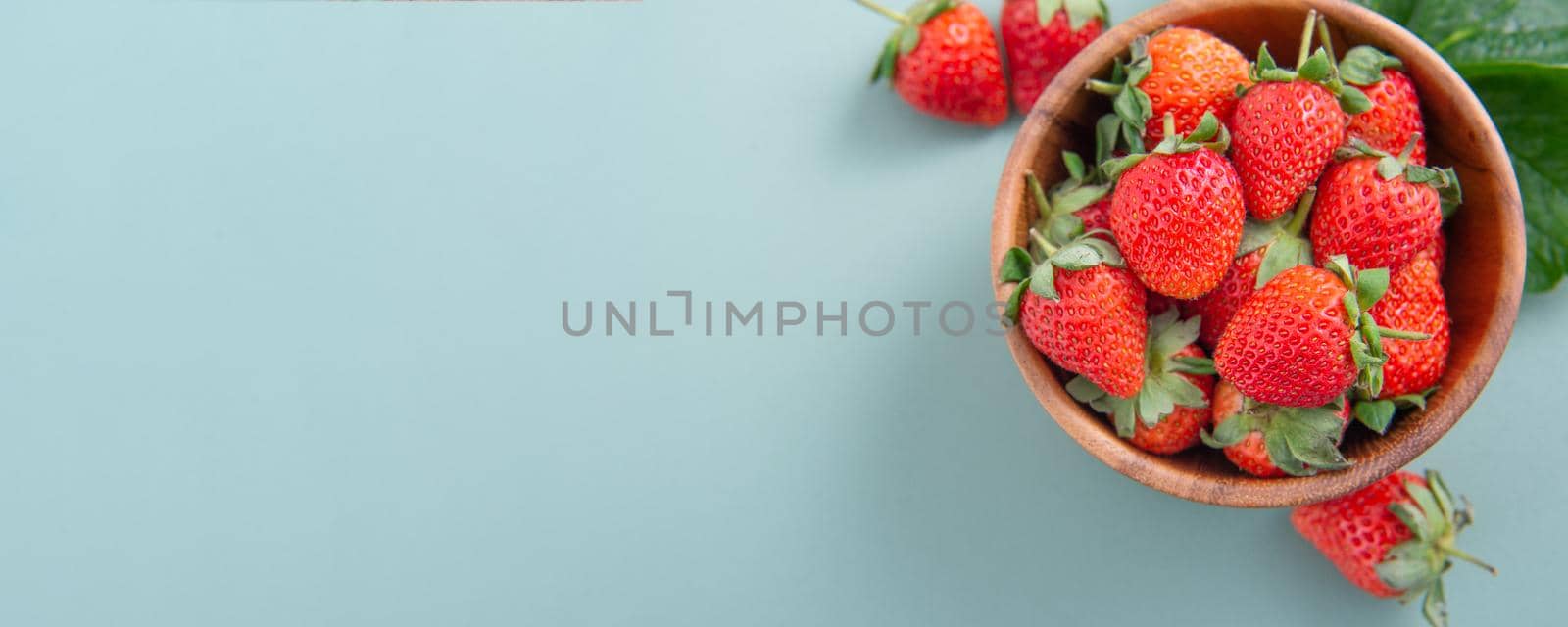 A bowl of beautiful and delicious strawberries isolated on a blue-green background, closeup, topview, copyspace.