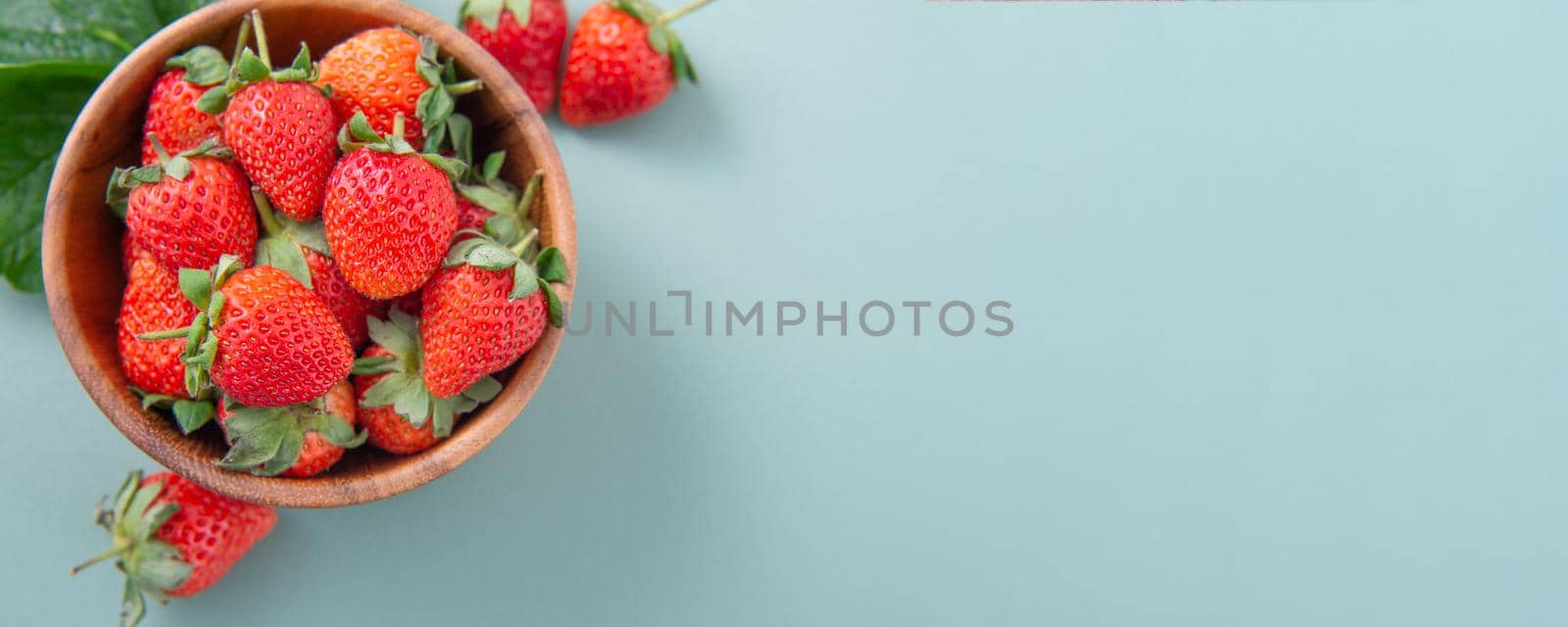 A bowl of beautiful and delicious strawberries isolated on a blue-green background, closeup, topview, copyspace.