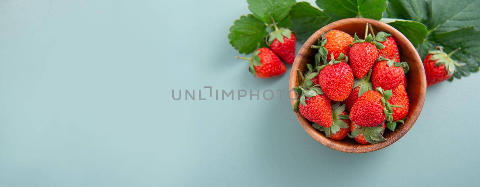 A bowl of beautiful and delicious strawberries isolated on a blue-green background, closeup, topview, copyspace.