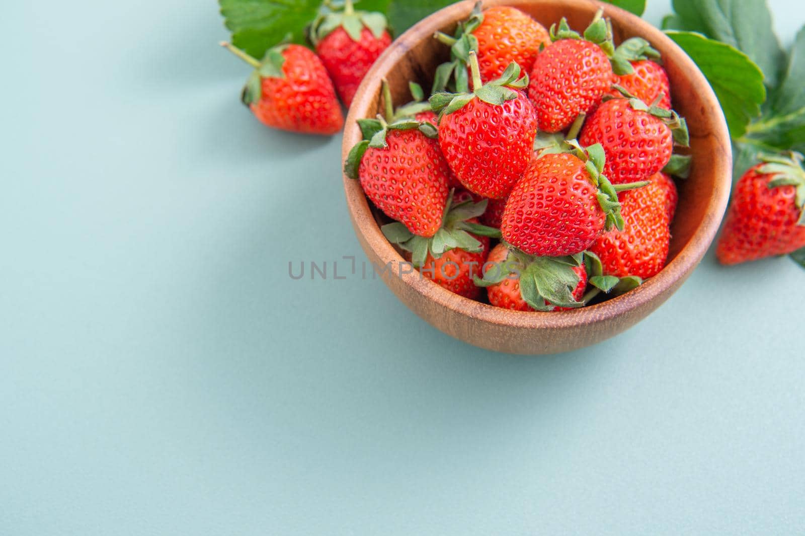 A bowl of beautiful and delicious strawberries isolated on a blue-green background, closeup, topview, copyspace.