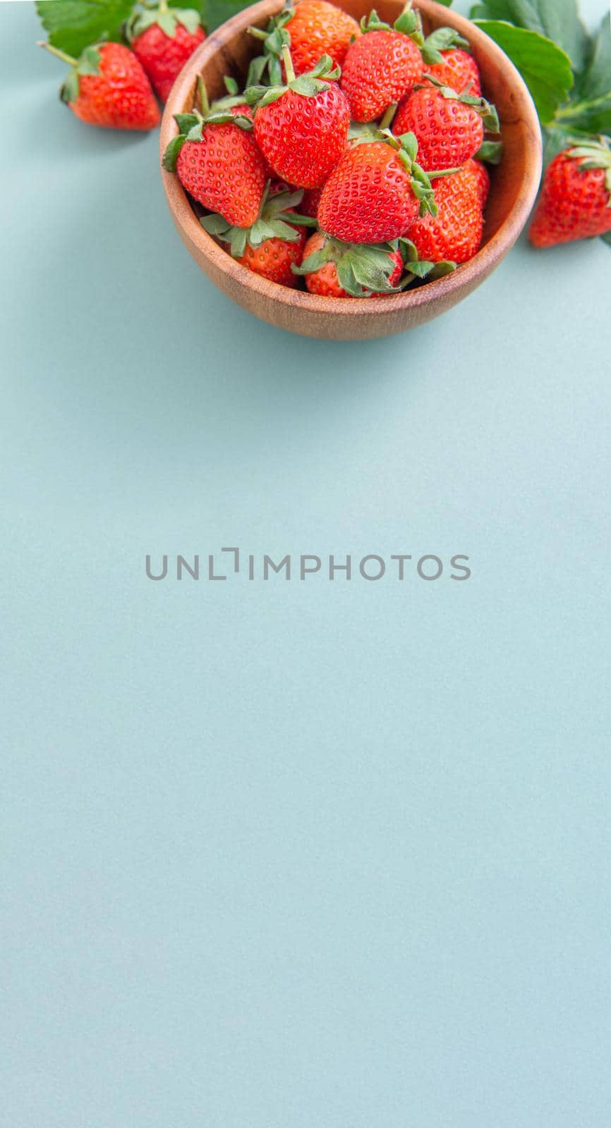 A bowl of beautiful and delicious strawberries isolated on a blue-green background, closeup, topview, copyspace.