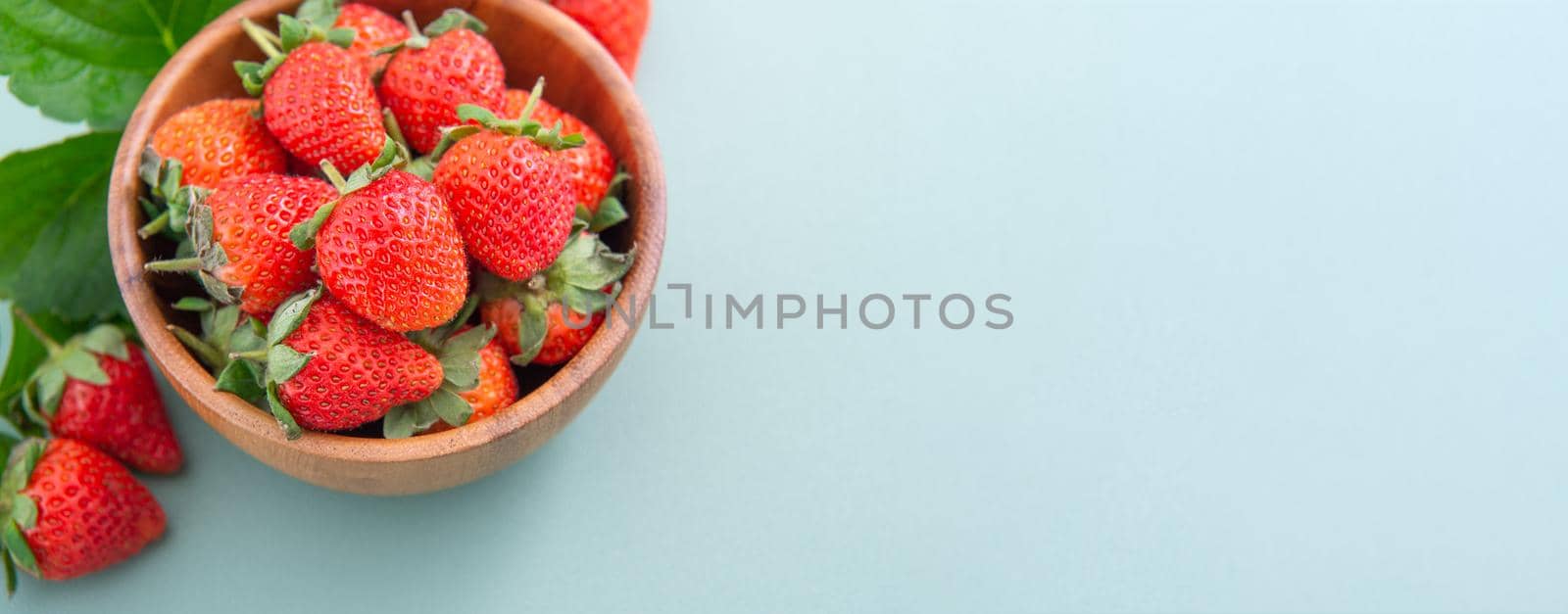 A bowl of beautiful and delicious strawberries isolated on a blue-green background, closeup, topview, copyspace.