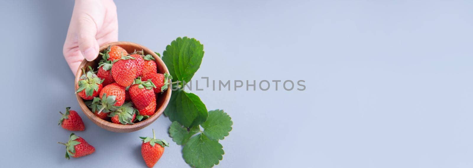 A young woman is holding a bowl of strawberries isolated on a airy blue background, closeup, topview, copyspace.