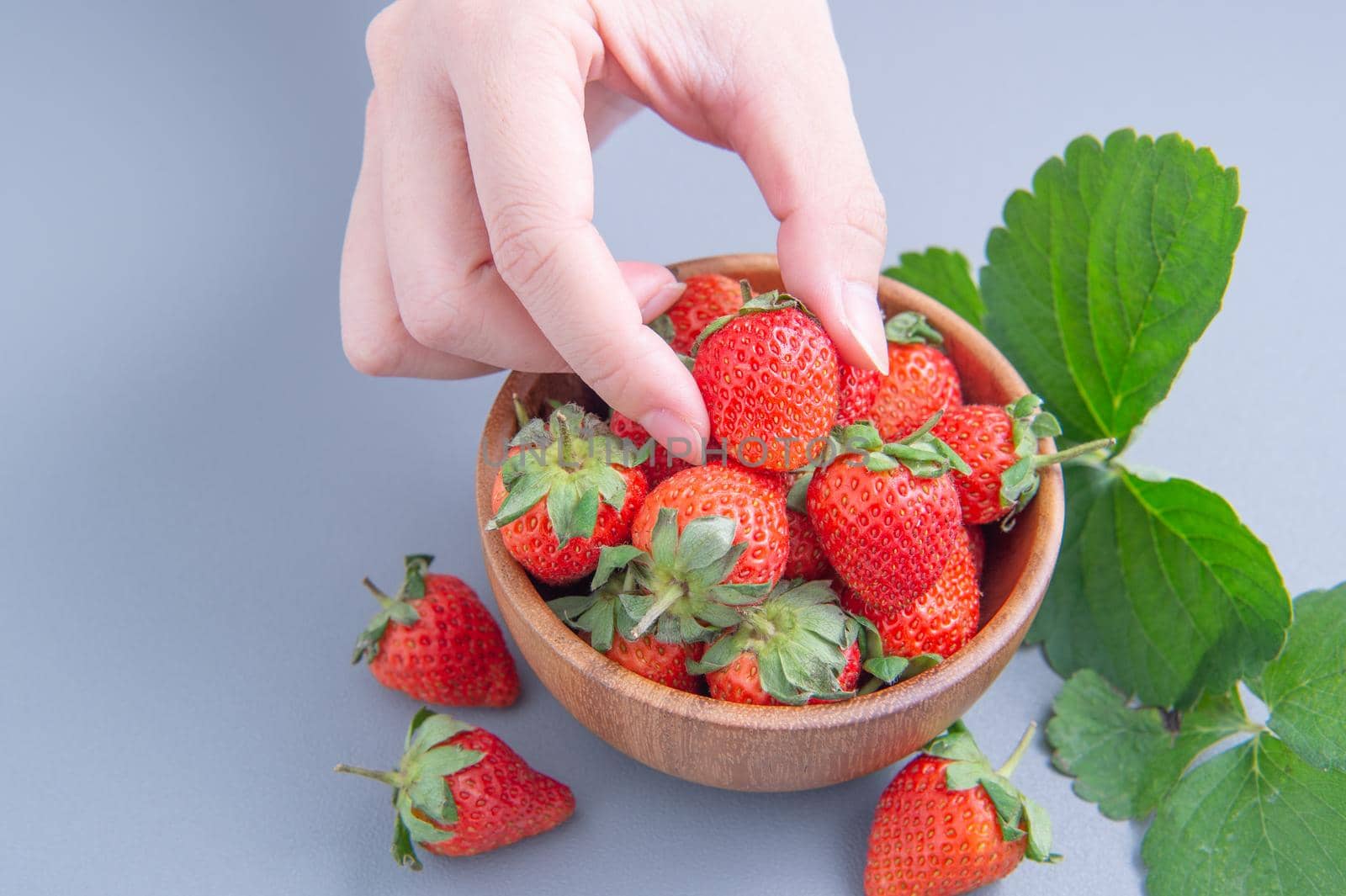 A young woman is holding a bowl of strawberries isolated on a airy blue background, closeup, topview, copyspace.