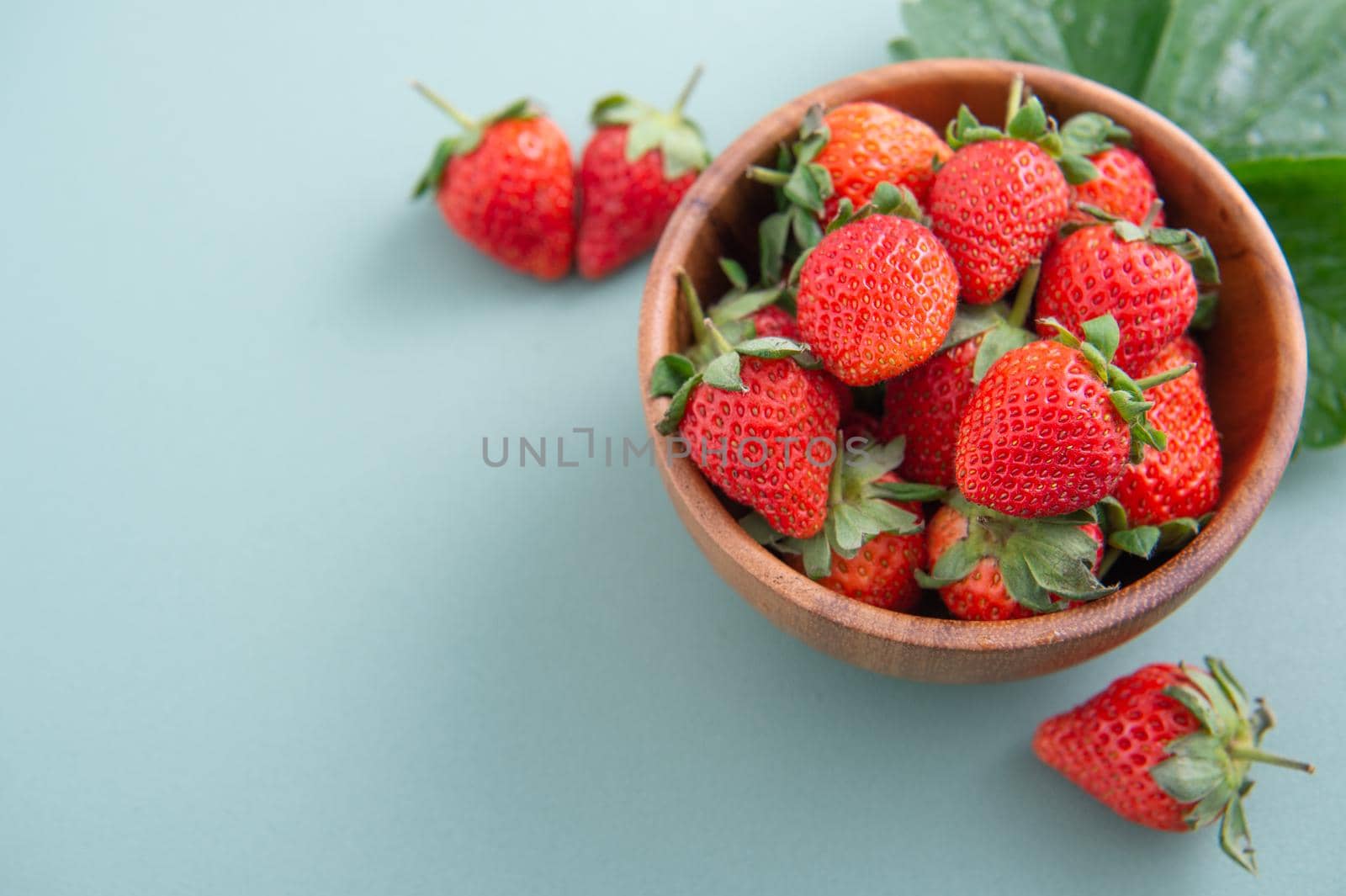 A bowl of beautiful and delicious strawberries isolated on a blue-green background, closeup, topview, copyspace.