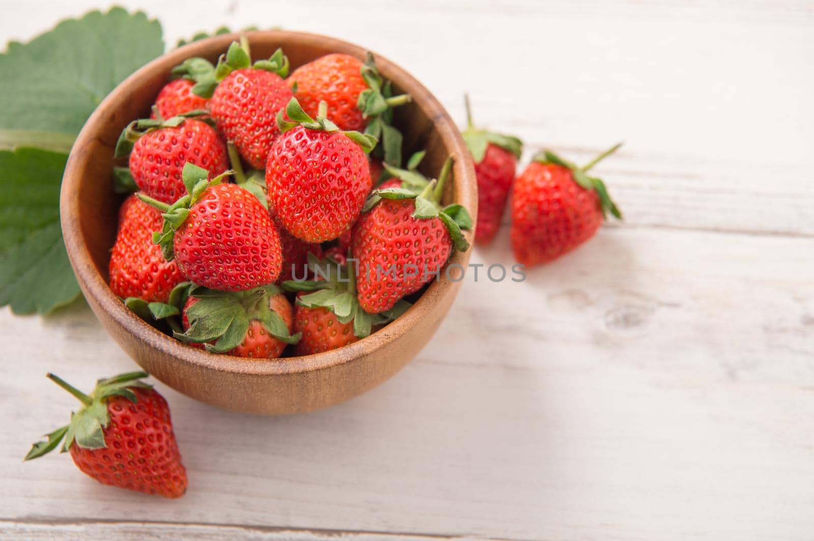 A bowl of beautiful and delicious strawberries isolated on a light wooden background, closeup, topview, copyspace.