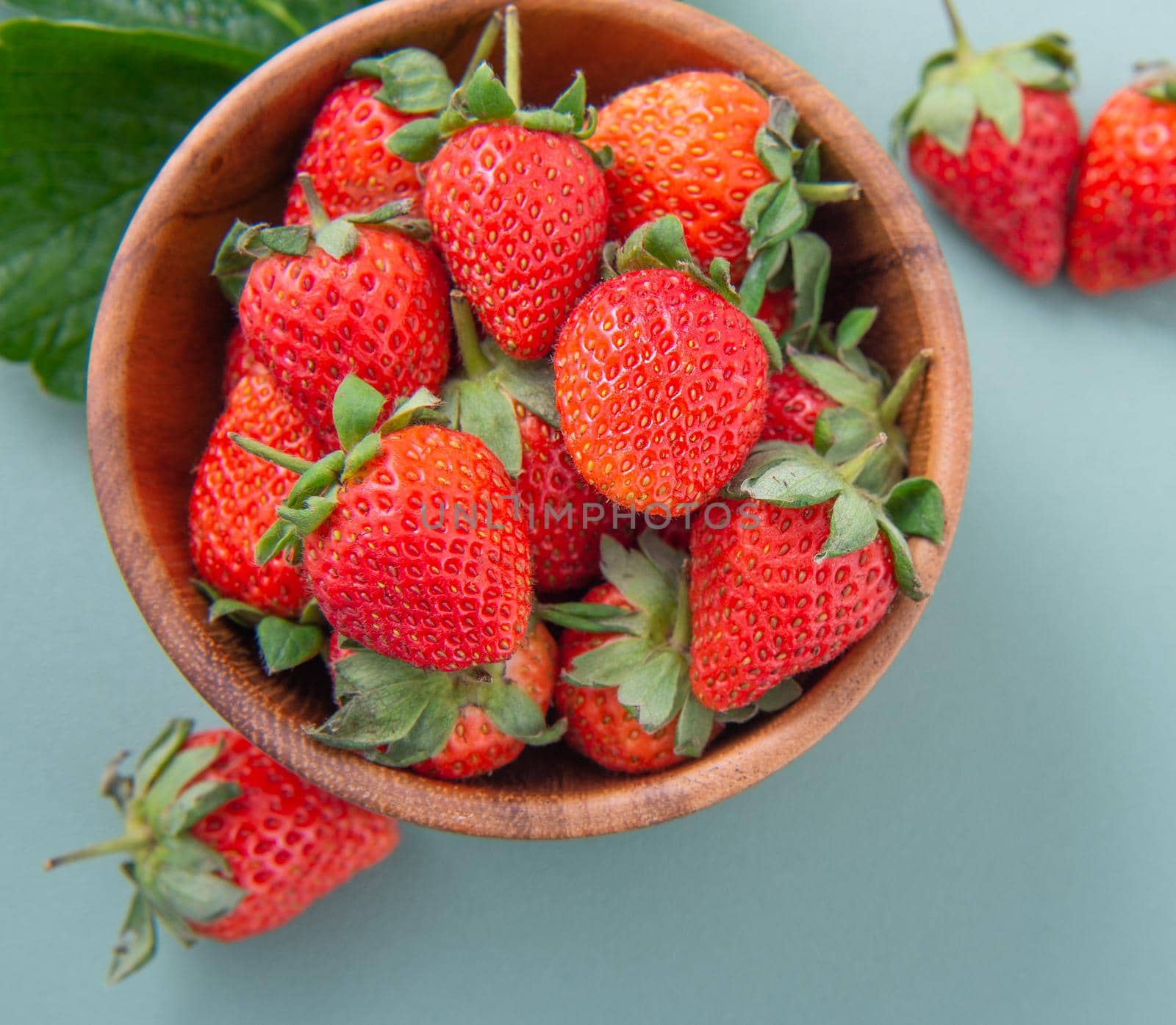 A bowl of beautiful and delicious strawberries isolated on a blue-green background, closeup, topview, copyspace.