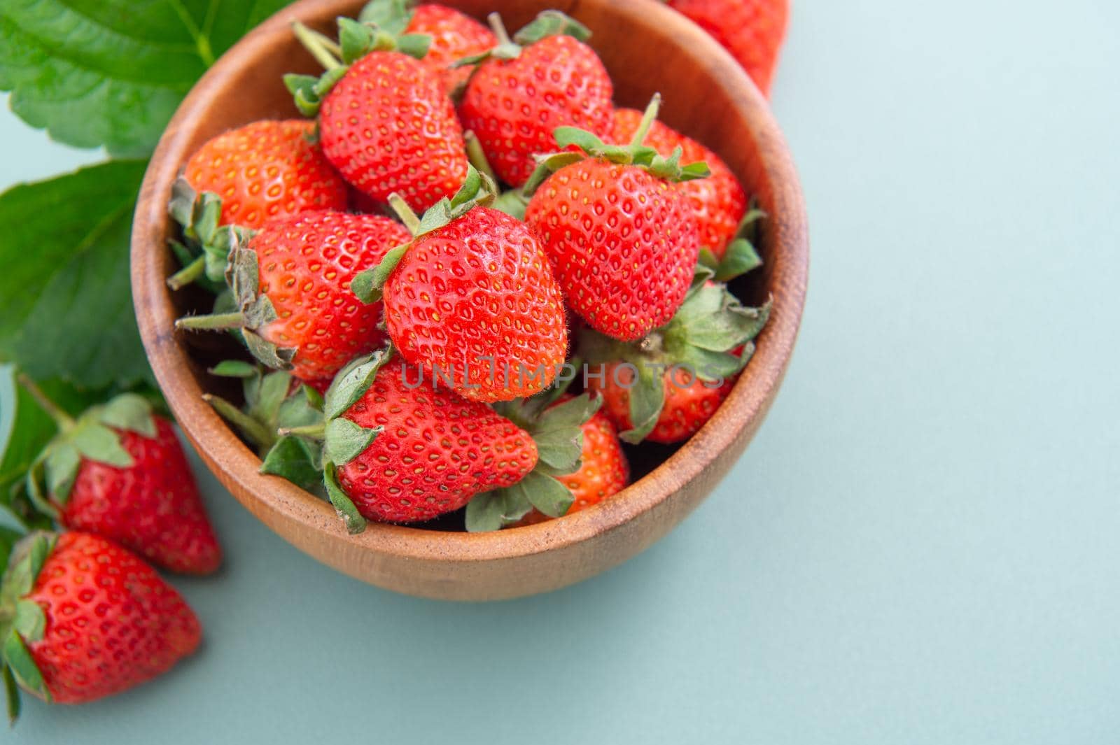 A bowl of beautiful and delicious strawberries isolated on a blue-green background, closeup, topview, copyspace.