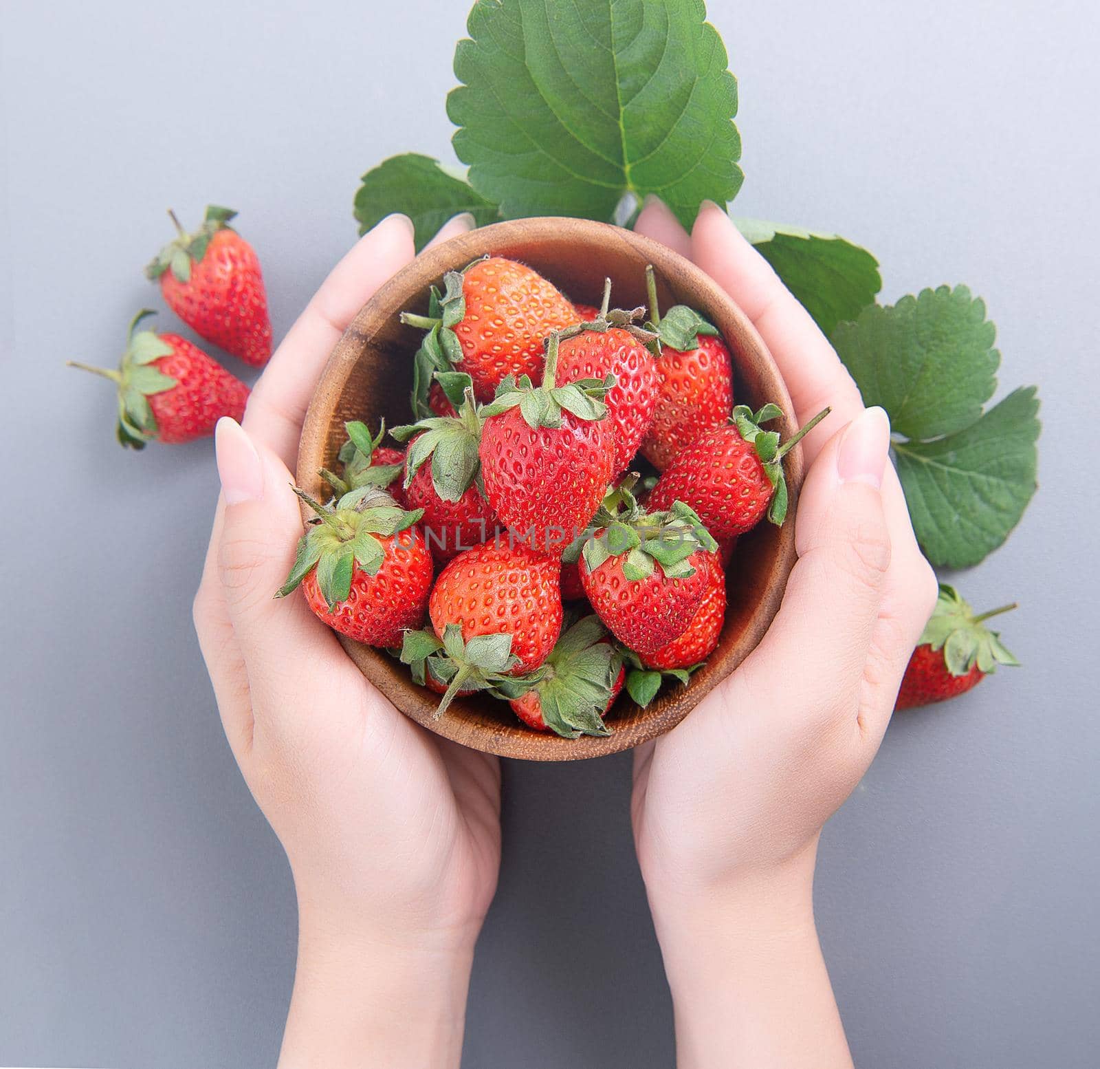 A young woman is holding a bowl of strawberries isolated on a airy blue background, closeup, topview, copyspace.