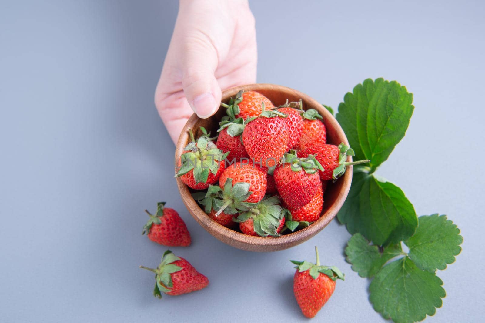 A young woman is holding a bowl of strawberries isolated on a airy blue background, closeup, topview, copyspace.