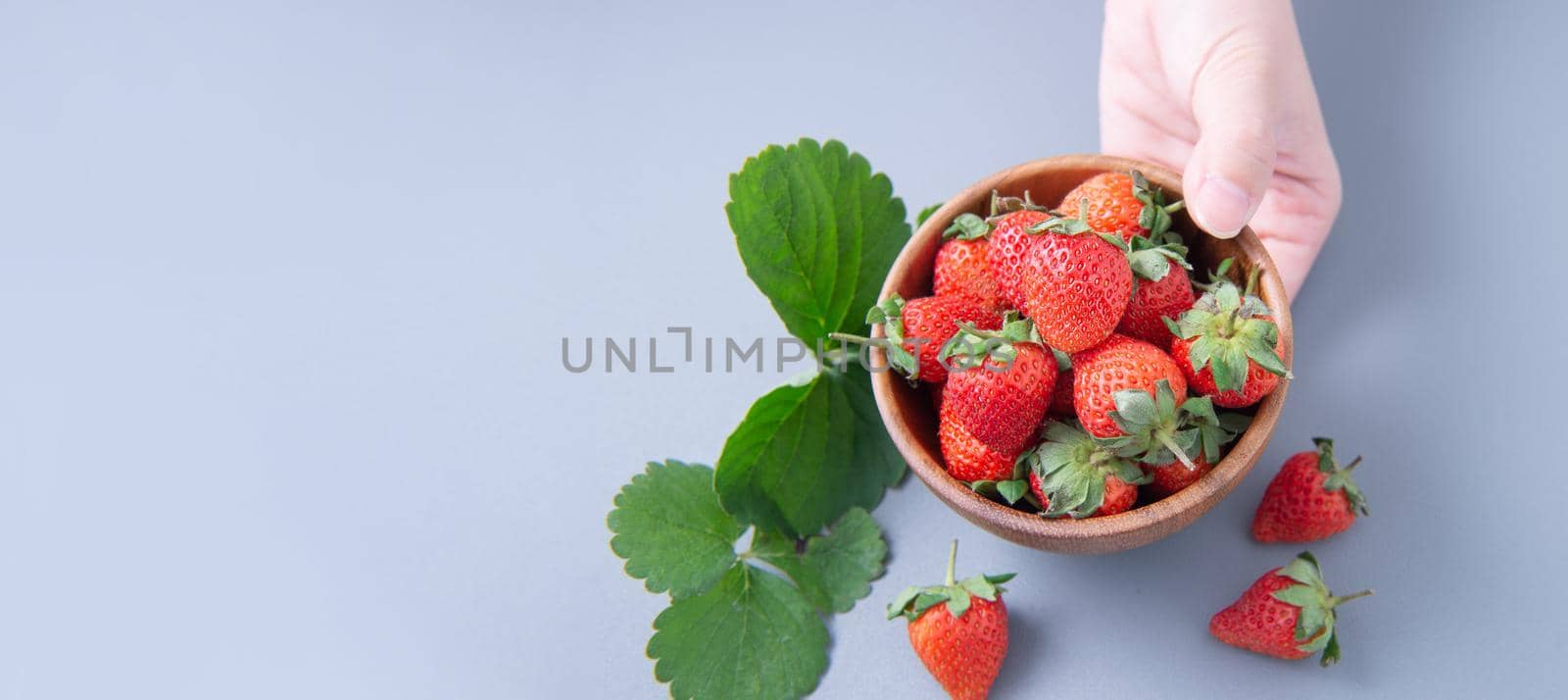 A young woman is holding a bowl of strawberries isolated on a airy blue background, closeup, topview, copyspace.