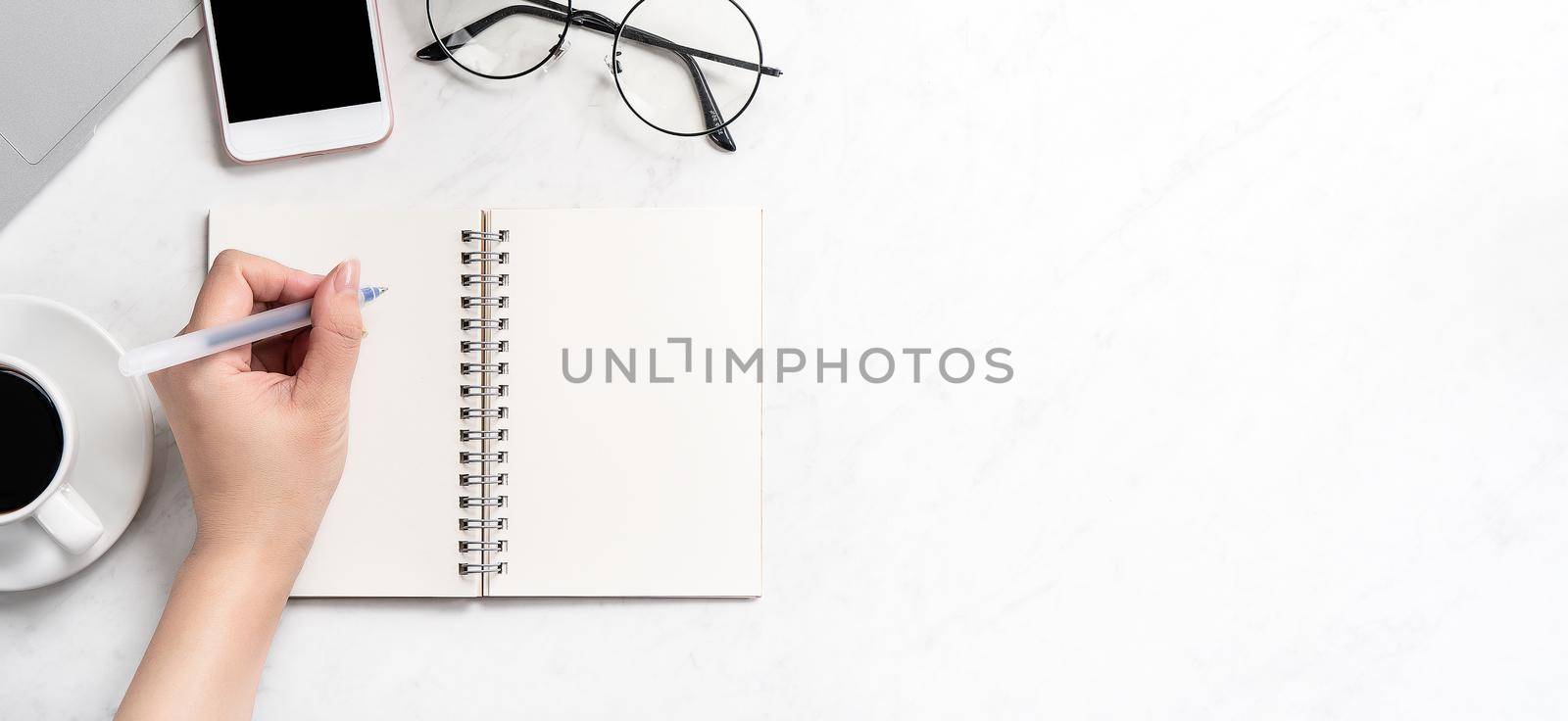 A woman is writing notes isolated on stylized marble office working desk with smartphone, laptop, glasses and coffee, mock up, topview, flatlay, copyspace, closeup