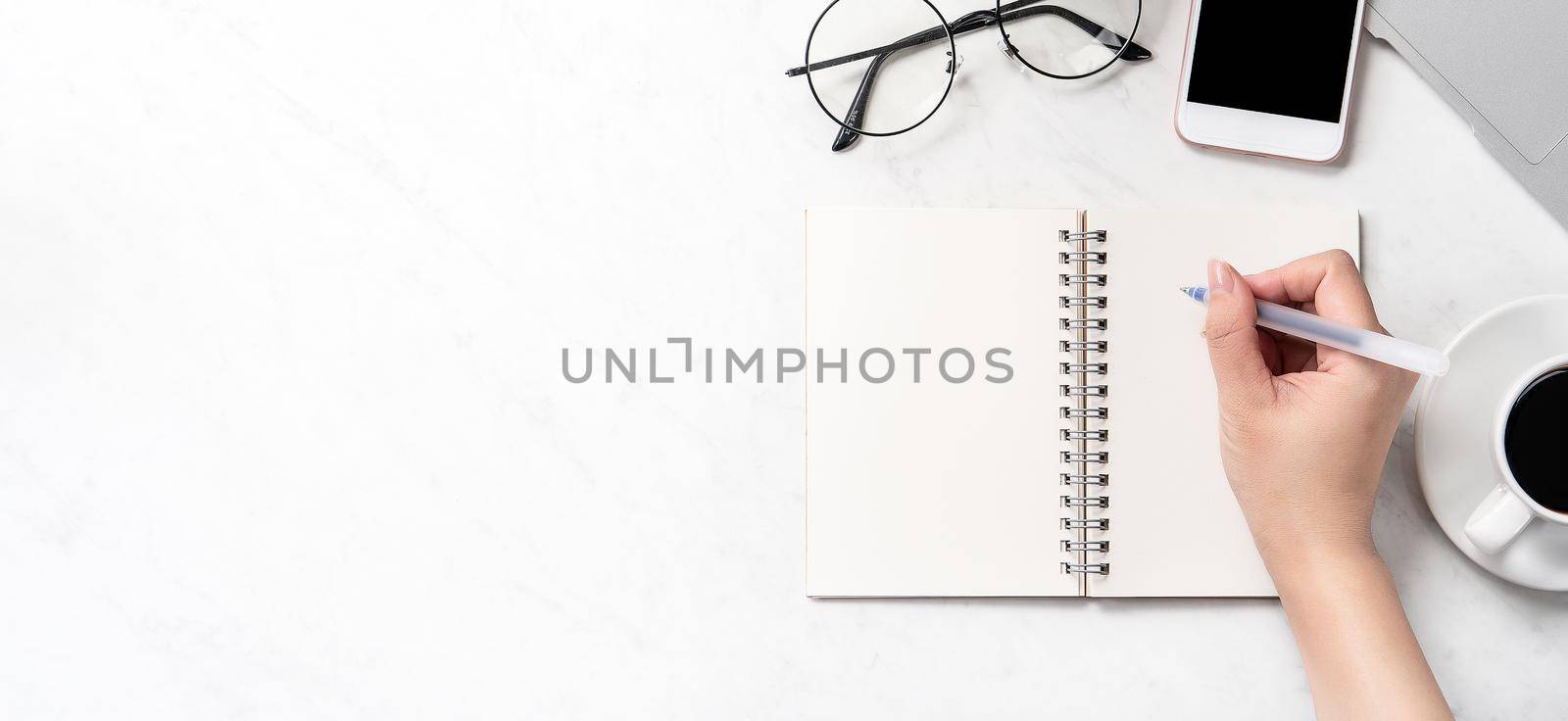 A woman is writing notes isolated on stylized marble office working desk with smartphone, laptop, glasses and coffee, mock up, topview, flatlay, copyspace, closeup