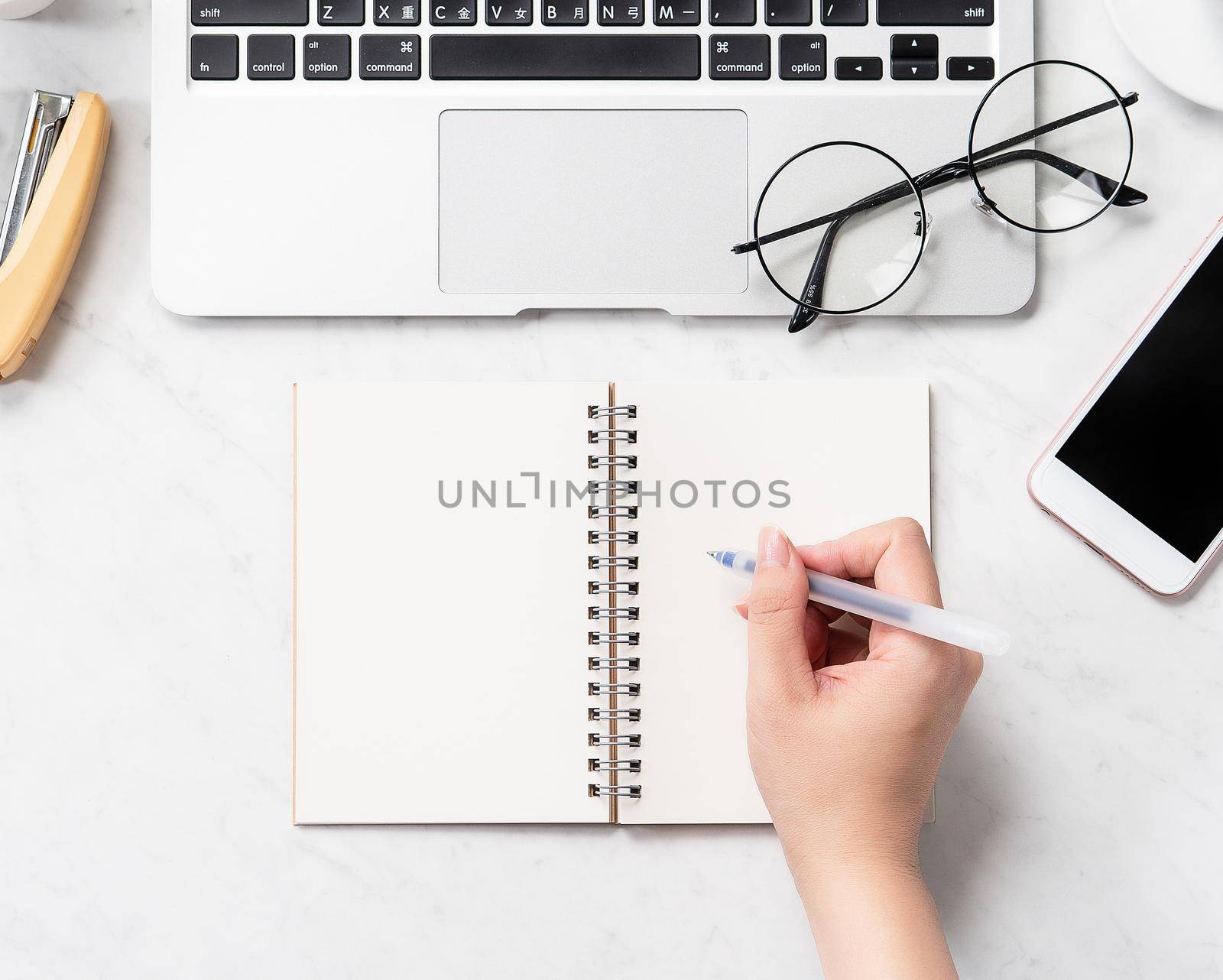 A woman is writing notes isolated on stylized marble office working desk with smartphone, laptop, glasses and coffee, mock up, topview, flatlay, copyspace, closeup