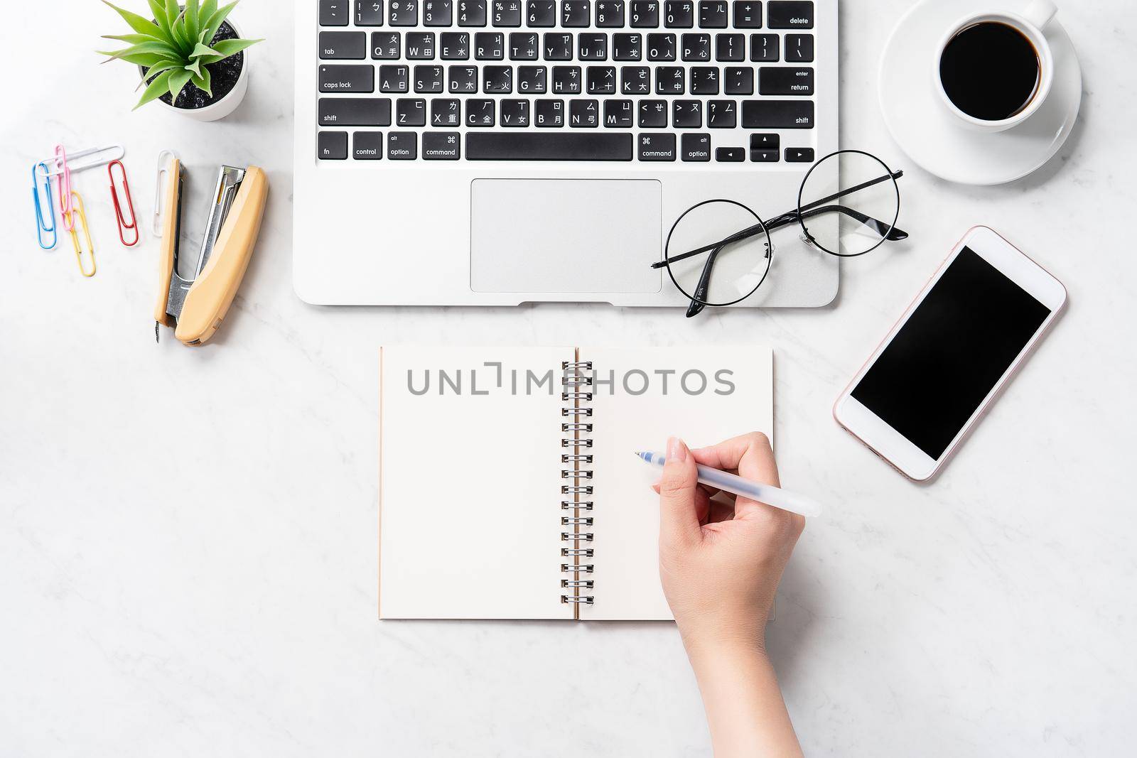 A woman is writing notes isolated on stylized marble office working desk with smartphone, laptop, glasses and coffee, mock up, topview, flatlay, copyspace, closeup