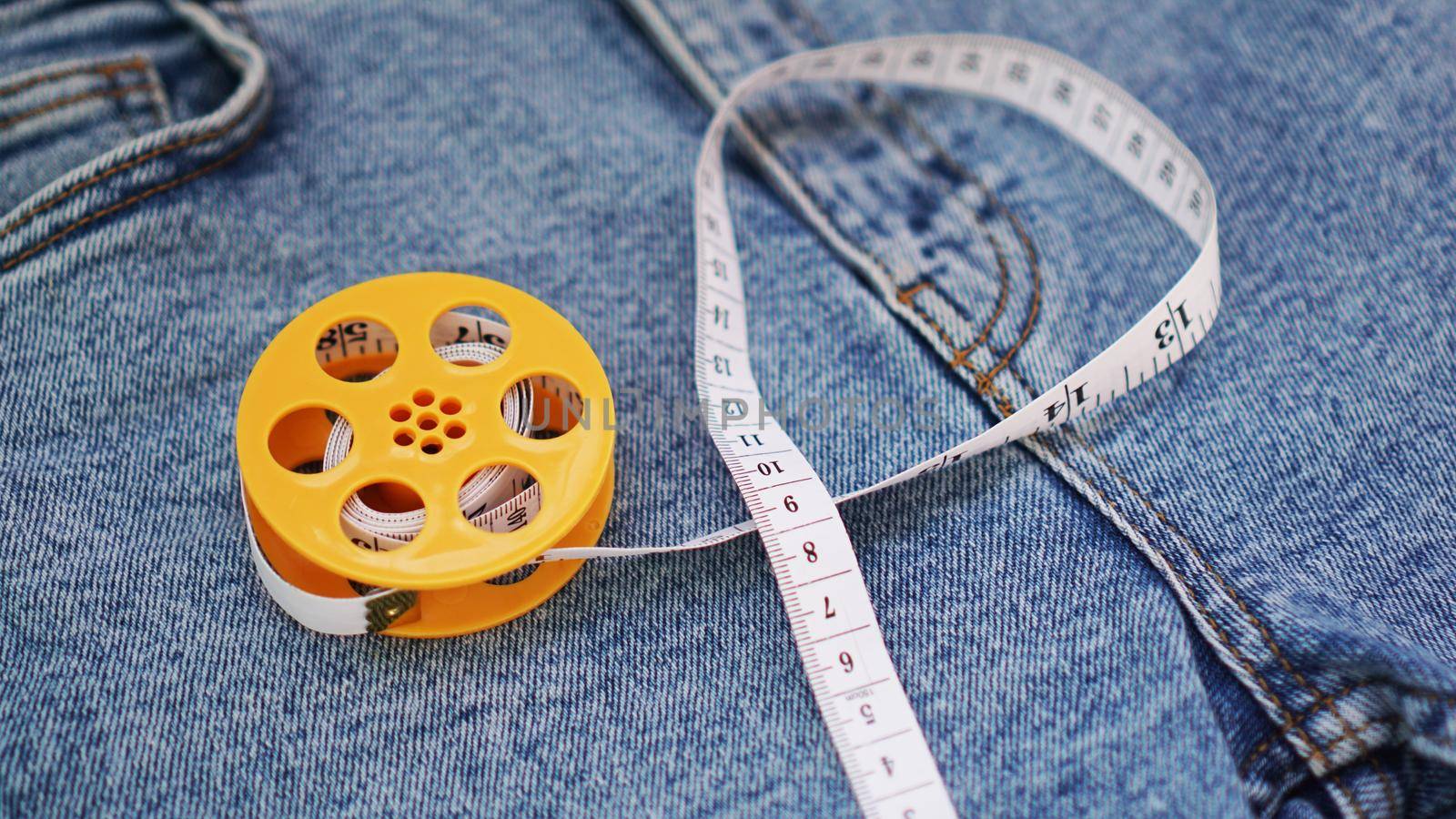 Blue jeans and a measuring tape. Slimming or sewing denim concept. Measuring tape in yellow spool on denim background