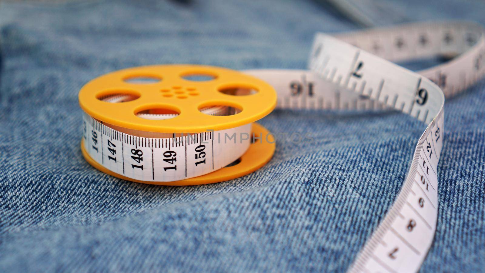 Blue jeans and a measuring tape. Slimming or sewing denim concept. Measuring tape in yellow spool on denim background