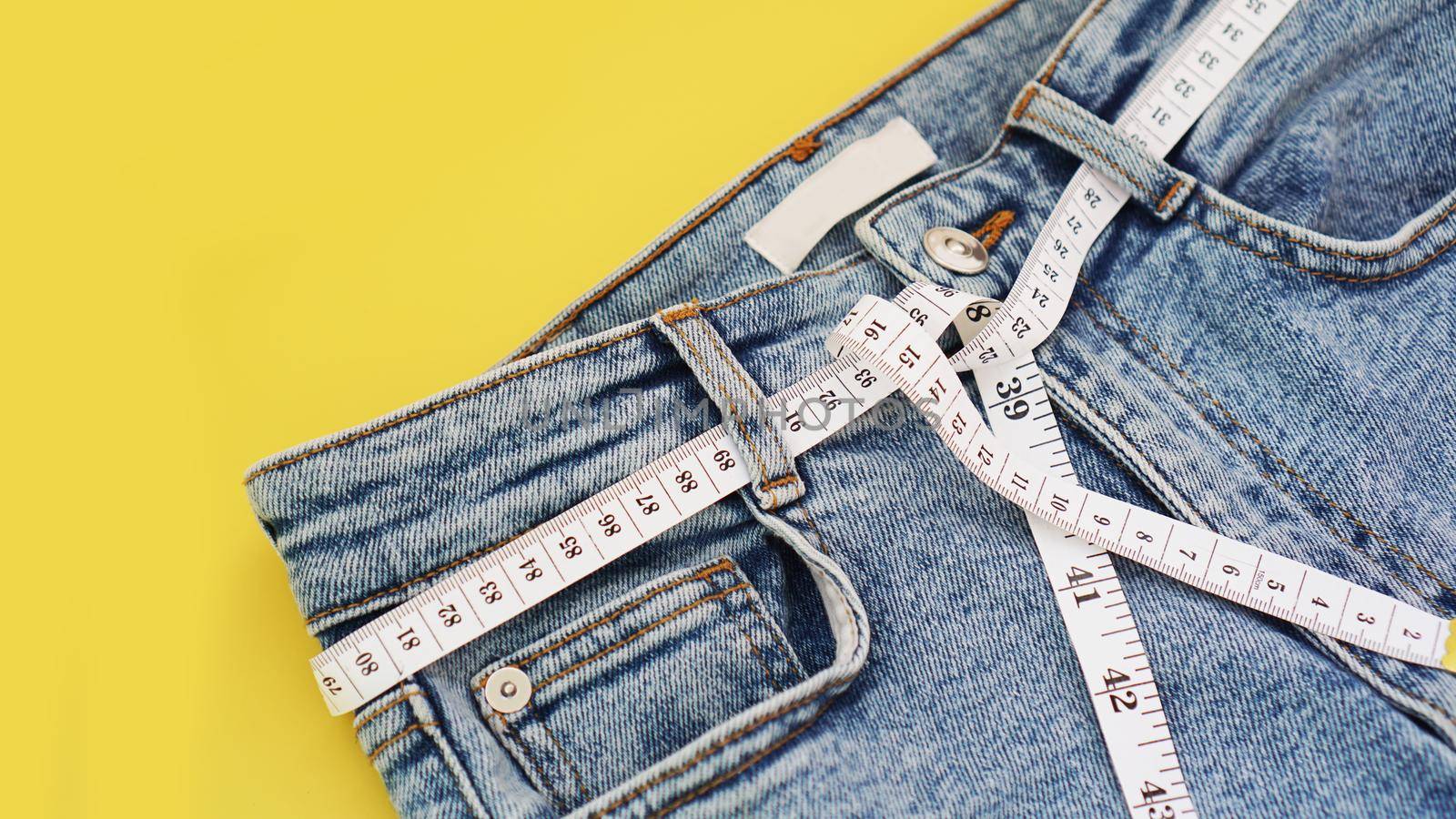 Measuring tape and jeans on a bright yellow background. Weight loss concept by summer