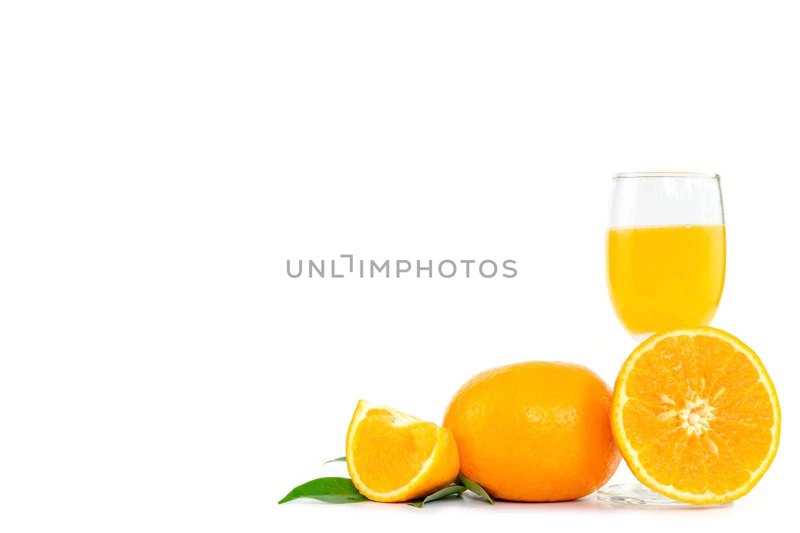 Freshly squeezed orange juice in a glass, decorated with citrus fruits and orange leaves on white background with copy space.