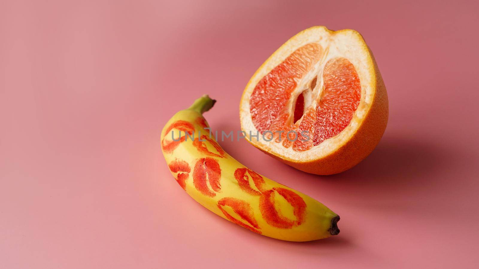 Composition with fresh banana with traces of red lipstick and grapefruit on pink background. Sex concept
