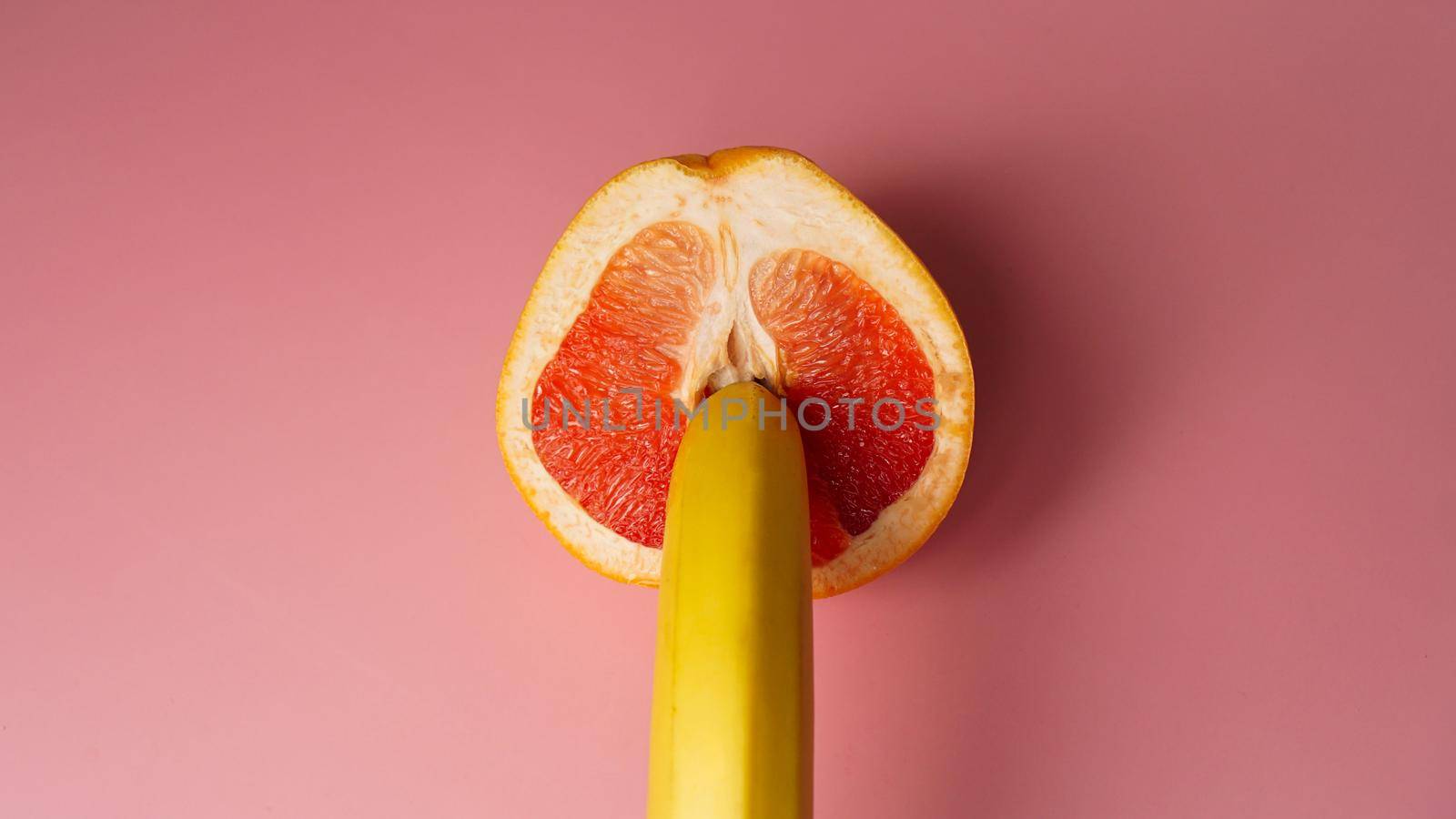 Banana with red grapefruit on pink background, sex concept