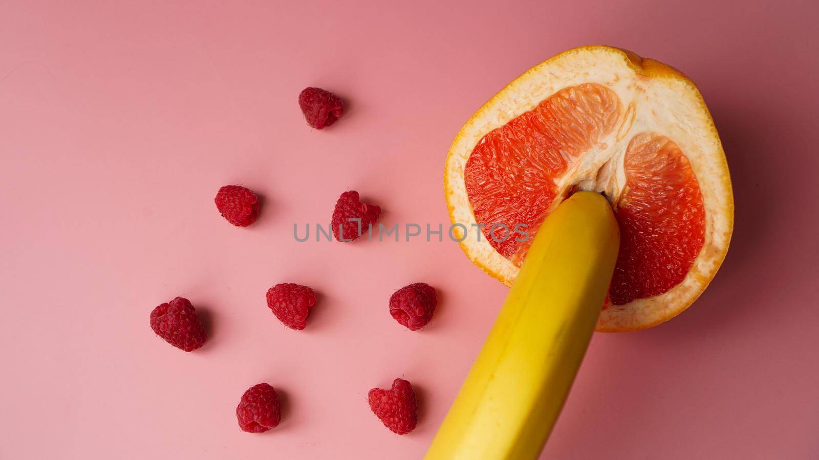 Banana with red grapefruit and raspberries on pink background, sex concept