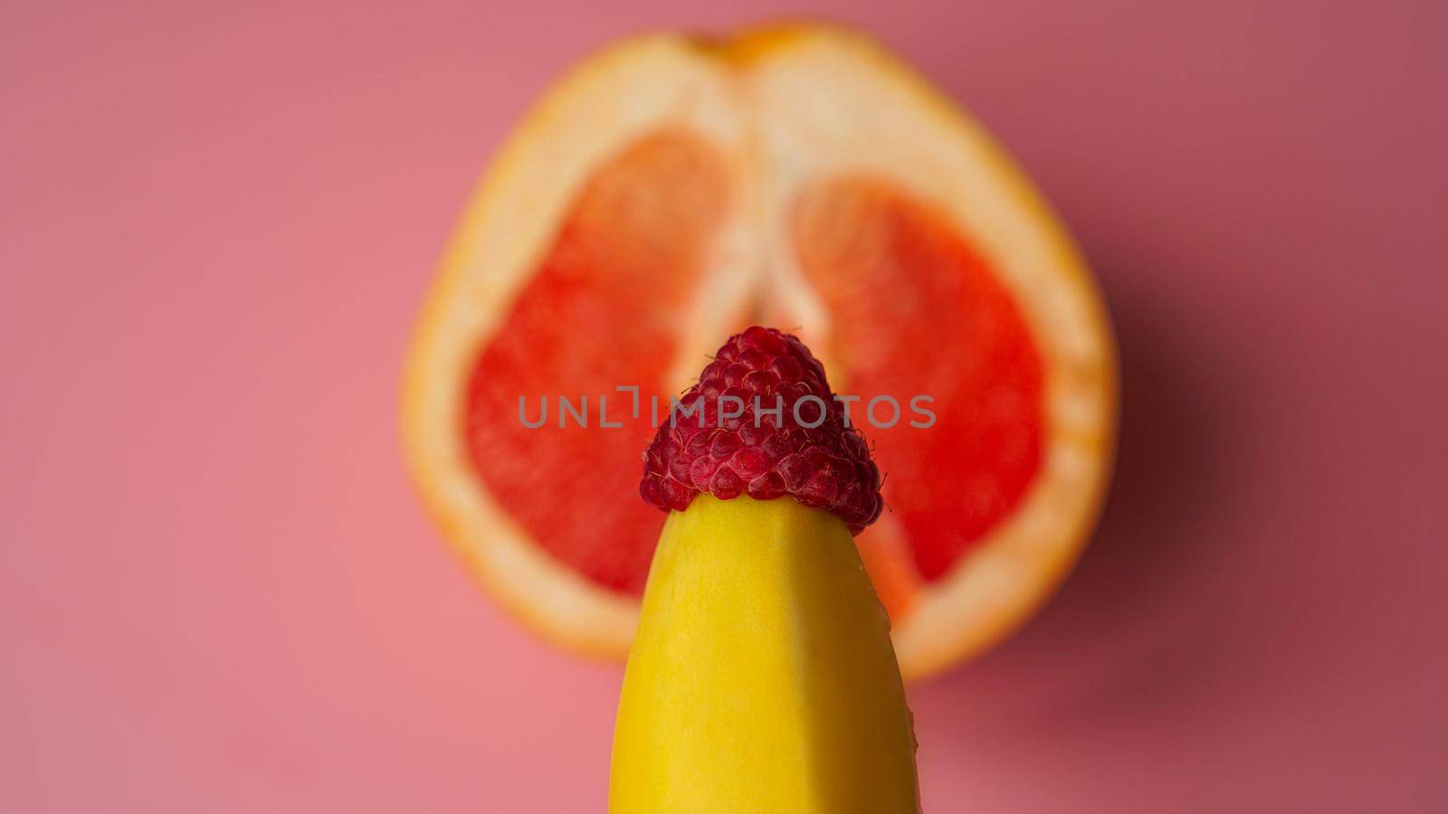 Banana with red grapefruit and raspberries on pink background, sex concept