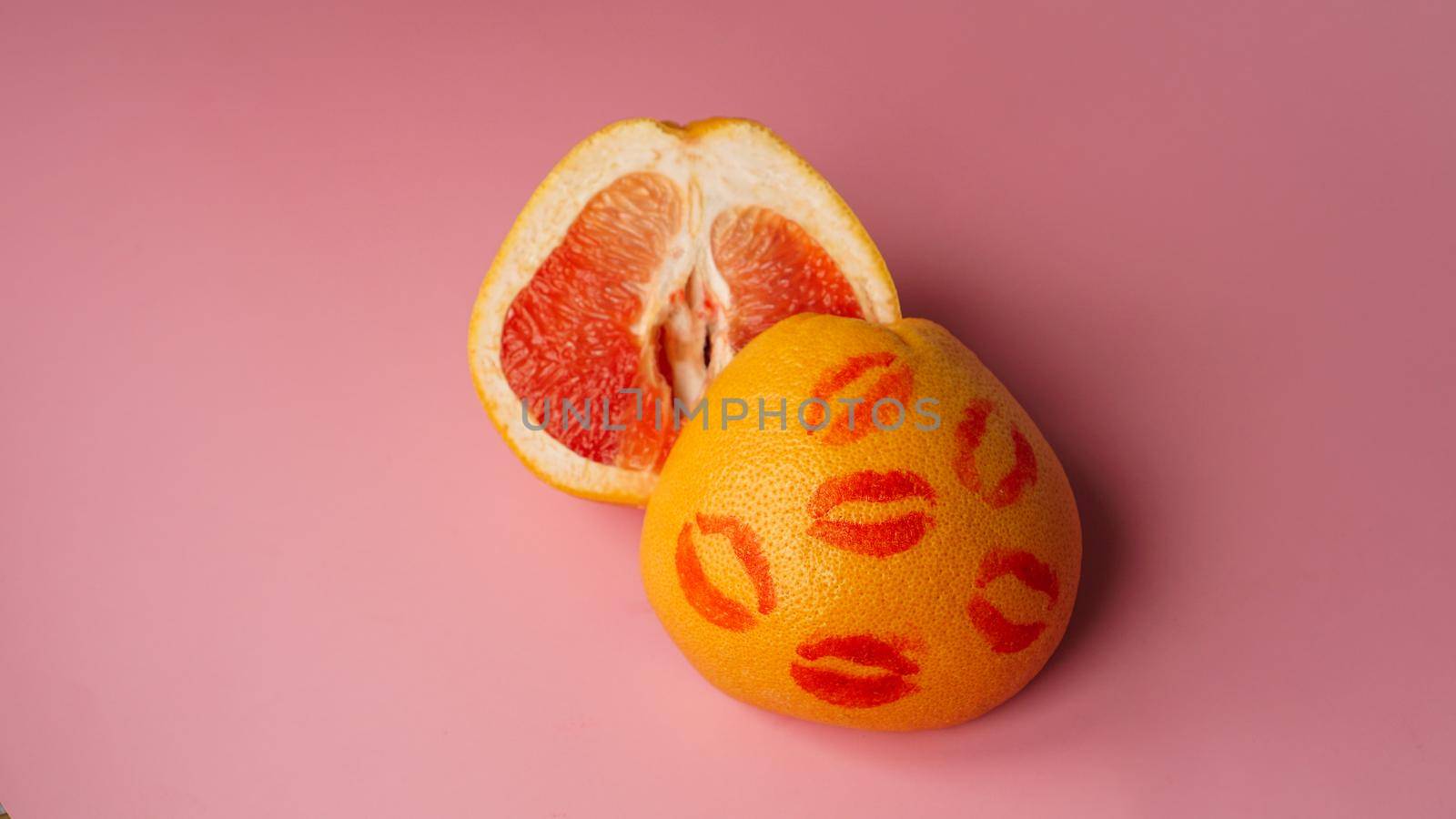 Composition with grapefruit with traces of red lipstick on pink background