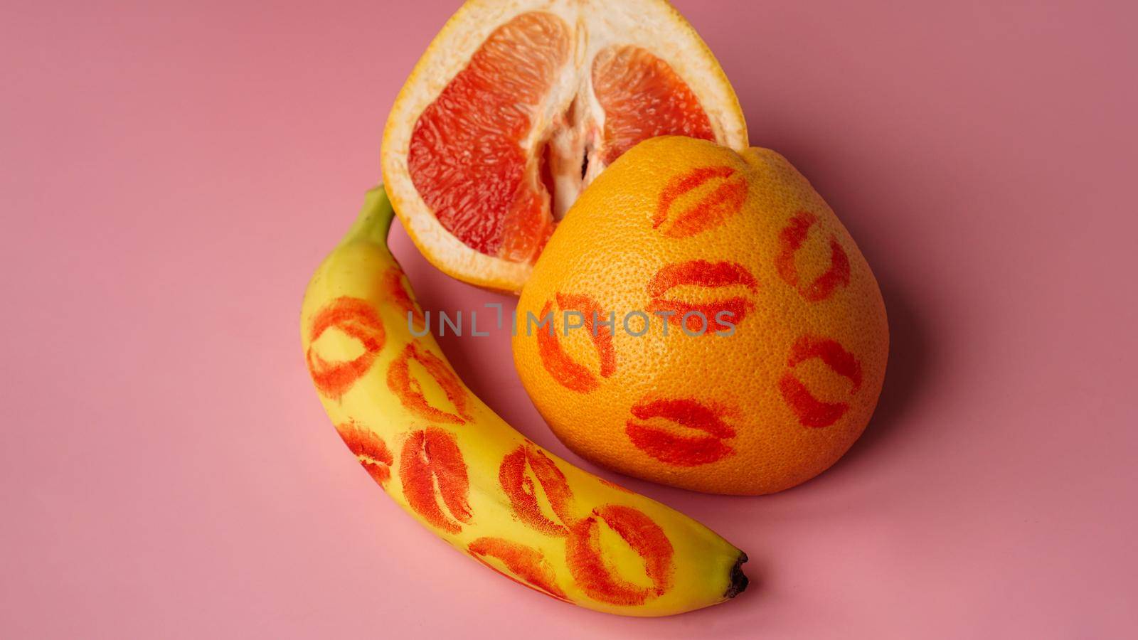 Composition with fresh banana and grapefruit with traces of red lipstick on pink background. Love concept