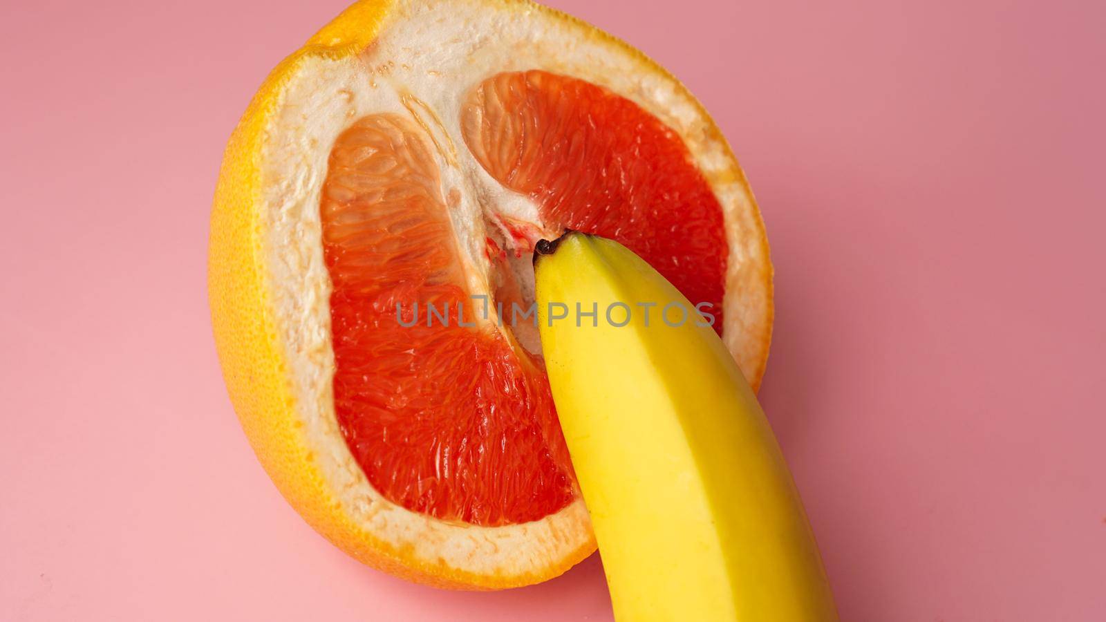 Banana with red grapefruit on pink background, sex concept