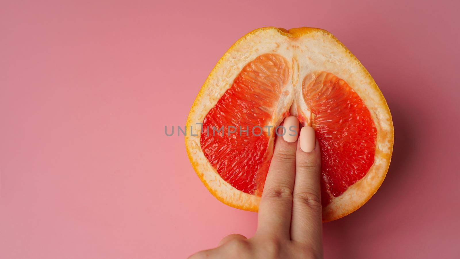 Vagina symbol. Fingers on grapefruit on pink background. by natali_brill