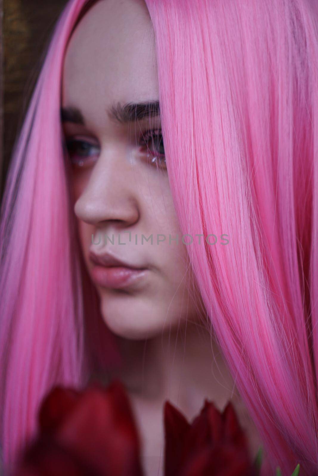 Close up fashion portrait. Vertical photo. Portrait of a dreamy girl with bright pink hair with flowers close to face. Looking to the side