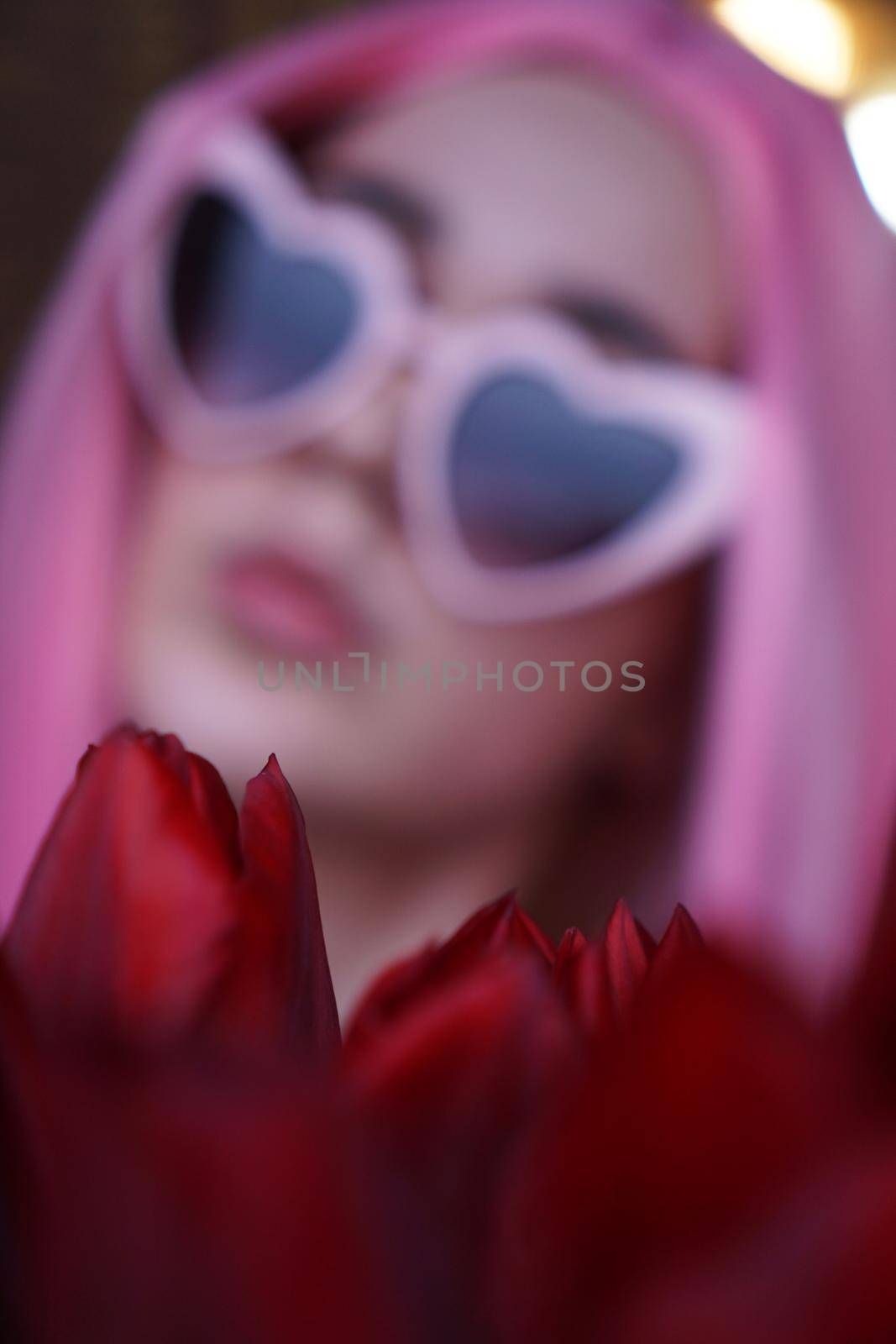 Out of focus, blurred background. Portrait of a dreamy girl with bright pink hair with flowers close to face. Looking to the side