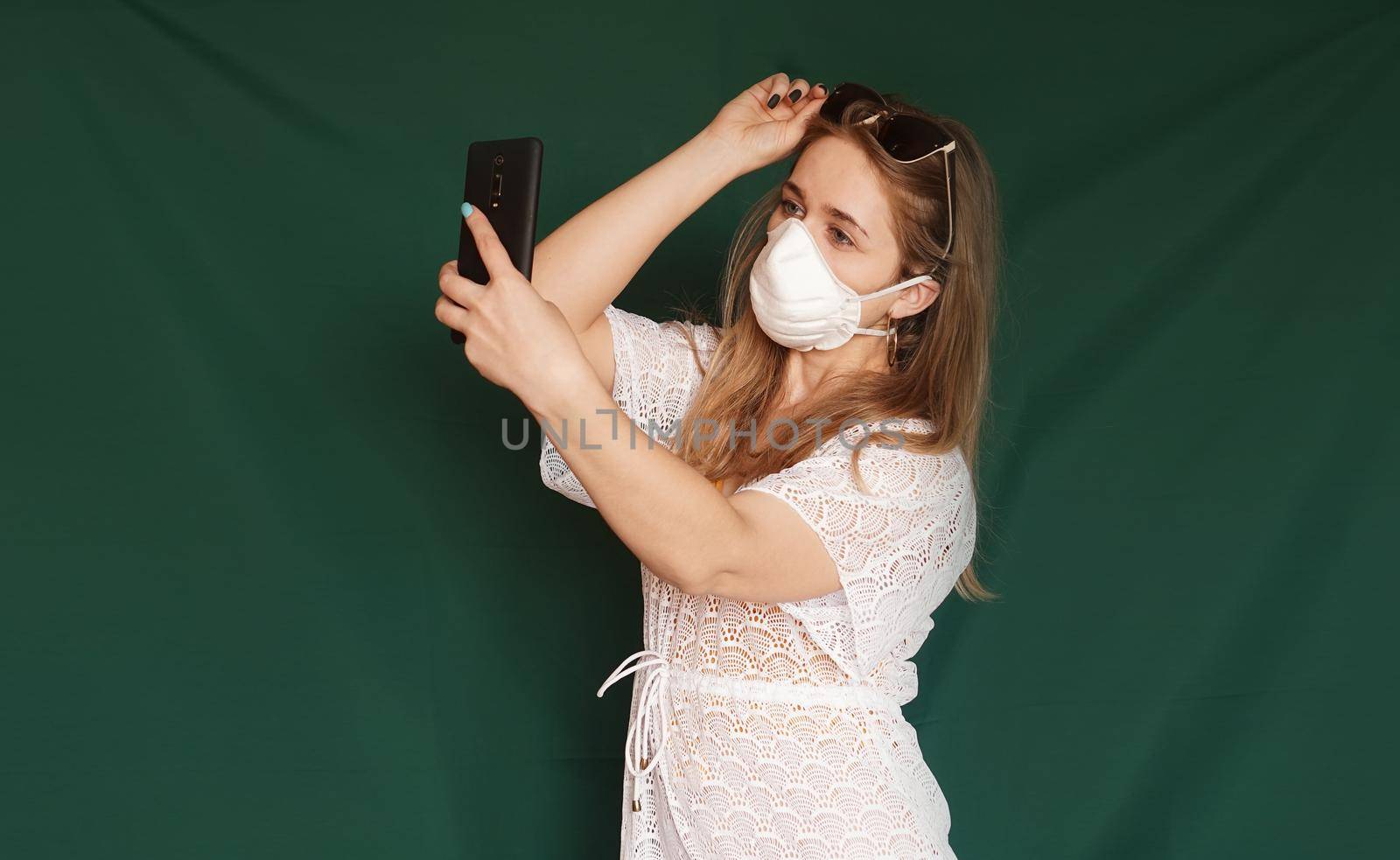 Beautiful girl in a white summer dress taking selfie . Medical mask on the face. Closed borders during coronavirus. Tourist