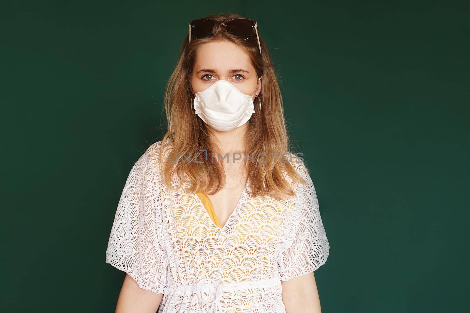 Beautiful girl in a white summer dress. Medical mask on the face. Closed borders during coronavirus. Tourist on a green background