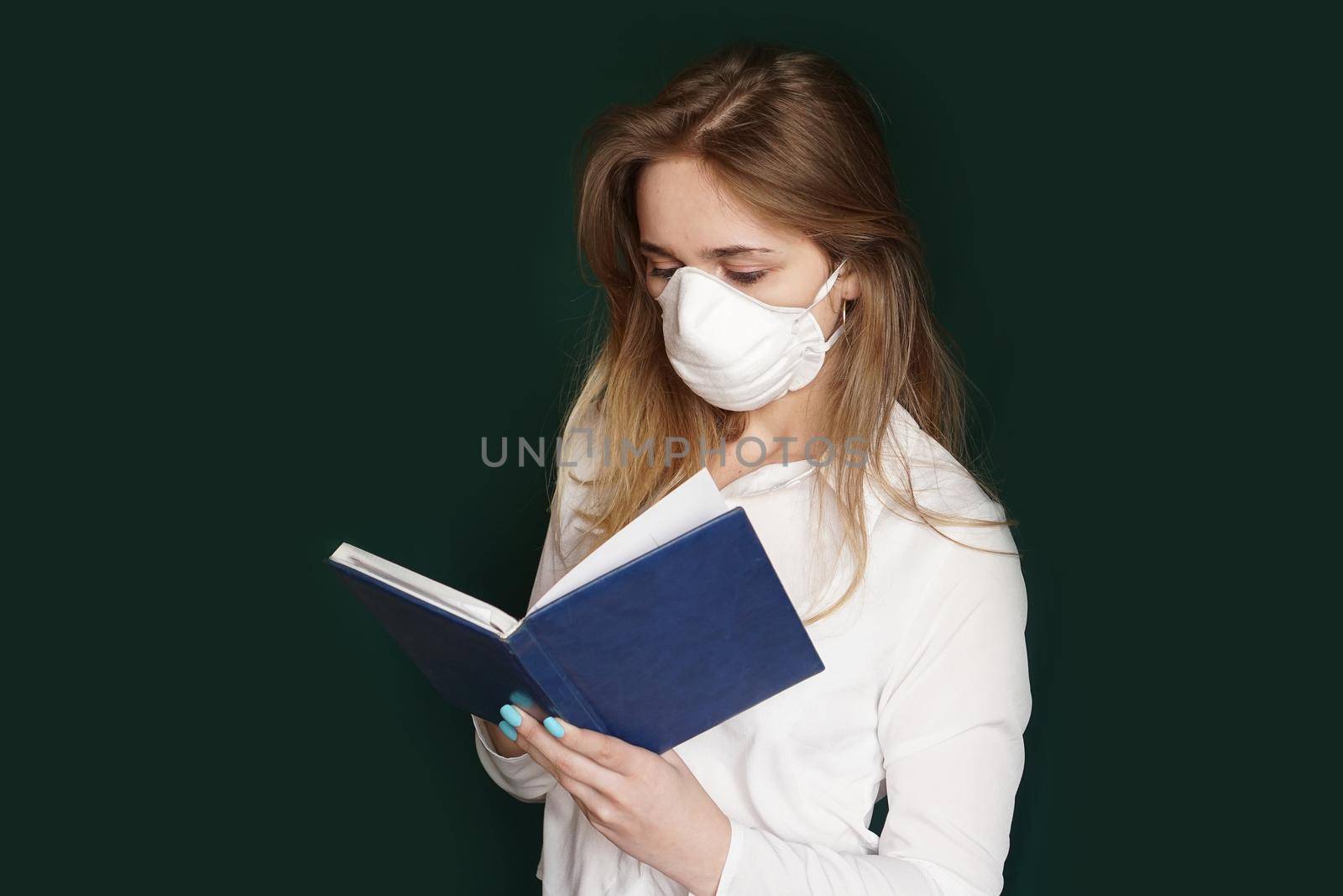 Young girl in a medical mask in a white office blouse with a notebook in hand on a green background