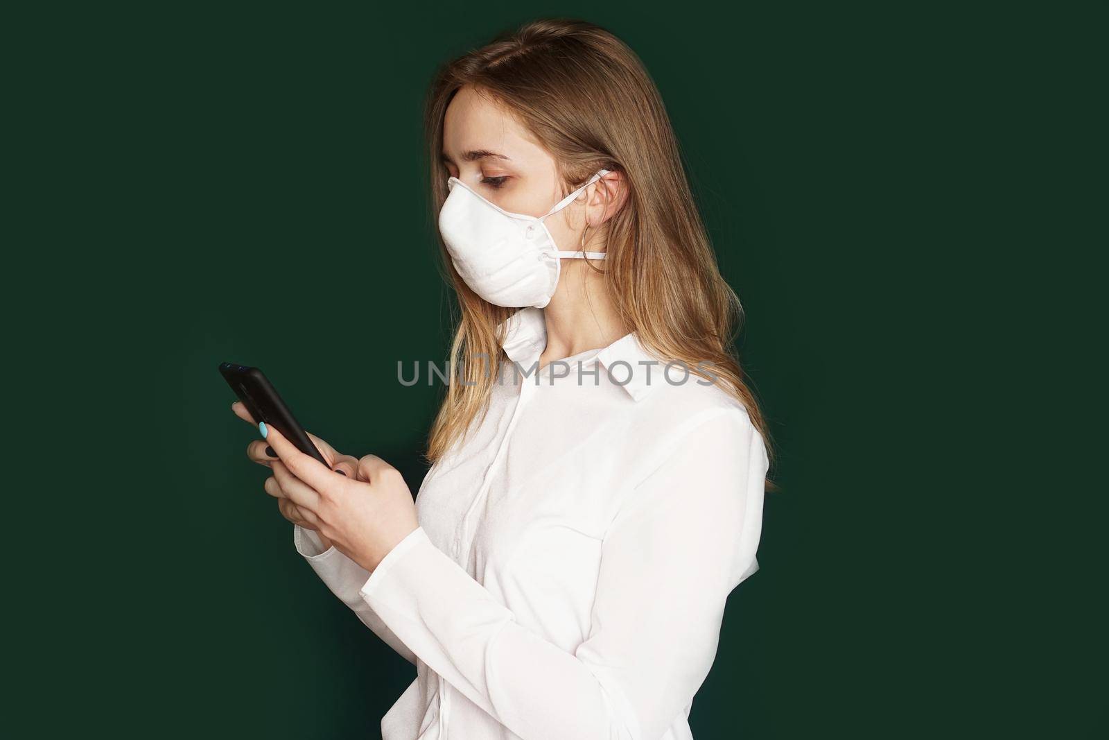 Girl in a medical mask, phone in hands, on a green background. COVID-19 outbreak of coronavirus. office concept