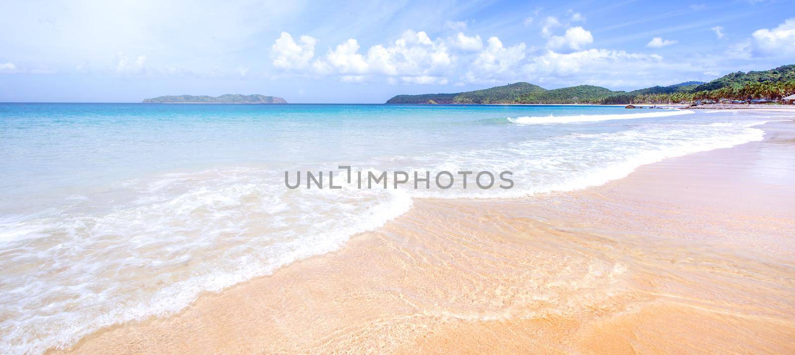 Beautiful amazing gold colored sandy beach with soft waves isolated with sunny blue sky. Concept of tropical calm tourism idea, copy space, close up