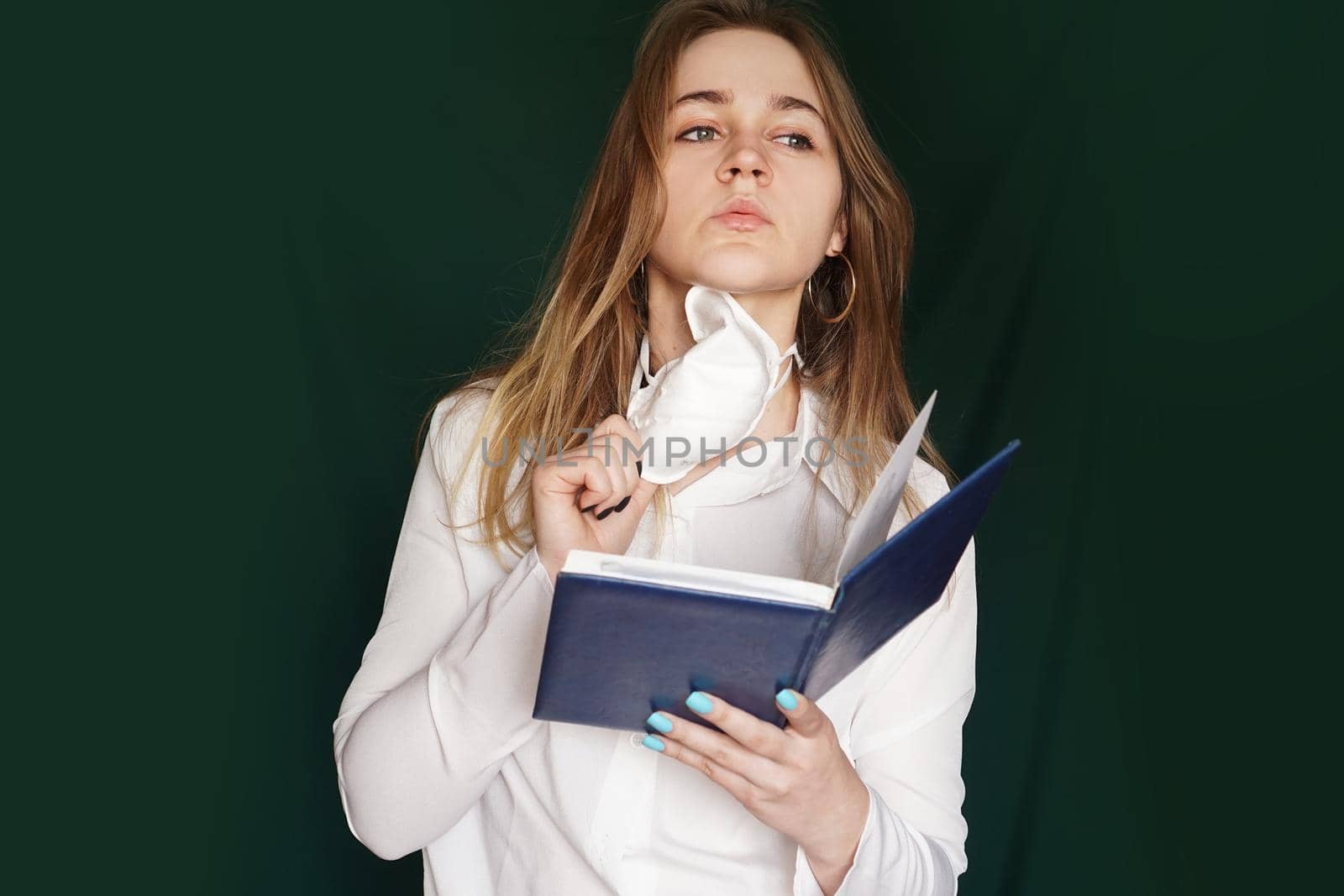 Young girl in a medical mask in a white office blouse with a notebook in hand on a green background